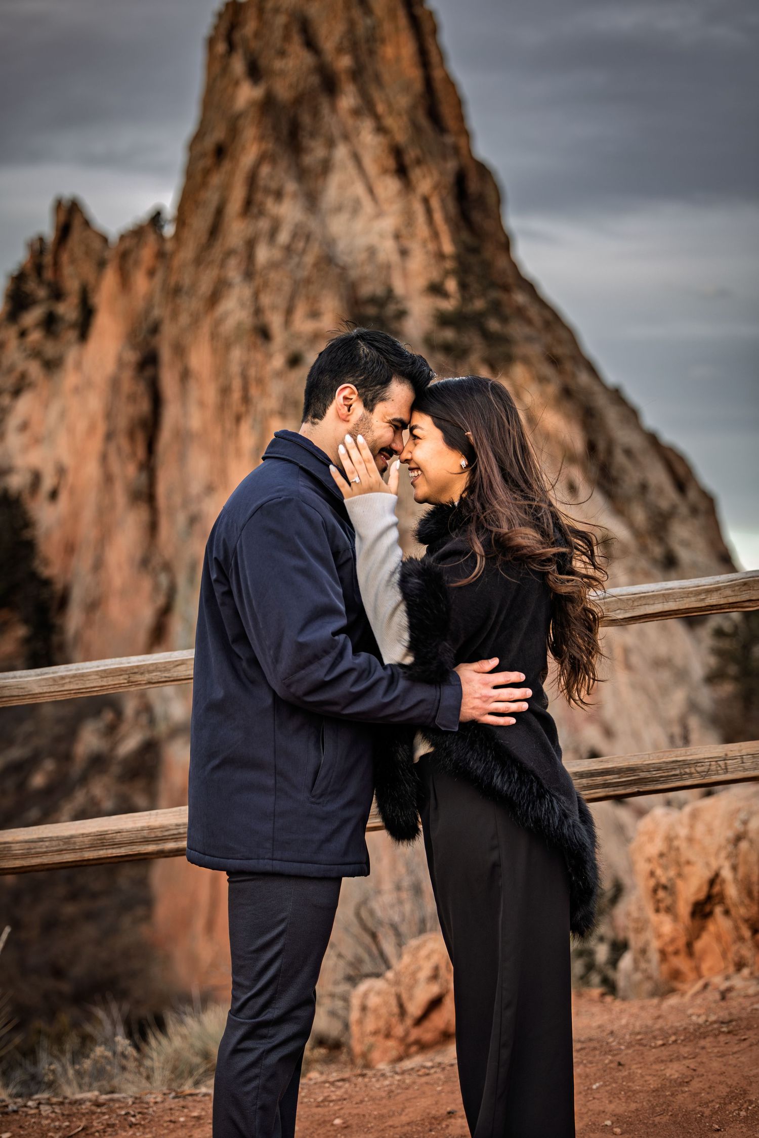 Couple embracing tenderly in front of dramatic rocky cliffs at Garden of the Gods during golden hour.