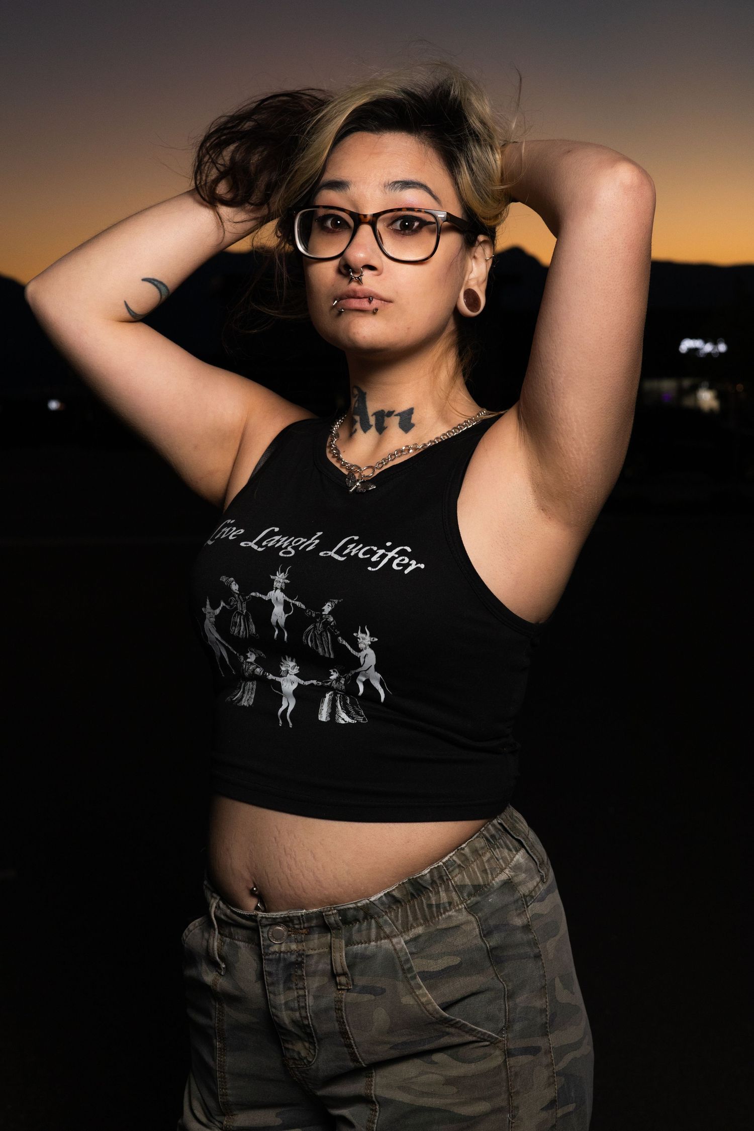 Portrait of a person in a crop top and camo pants posing at sunset.