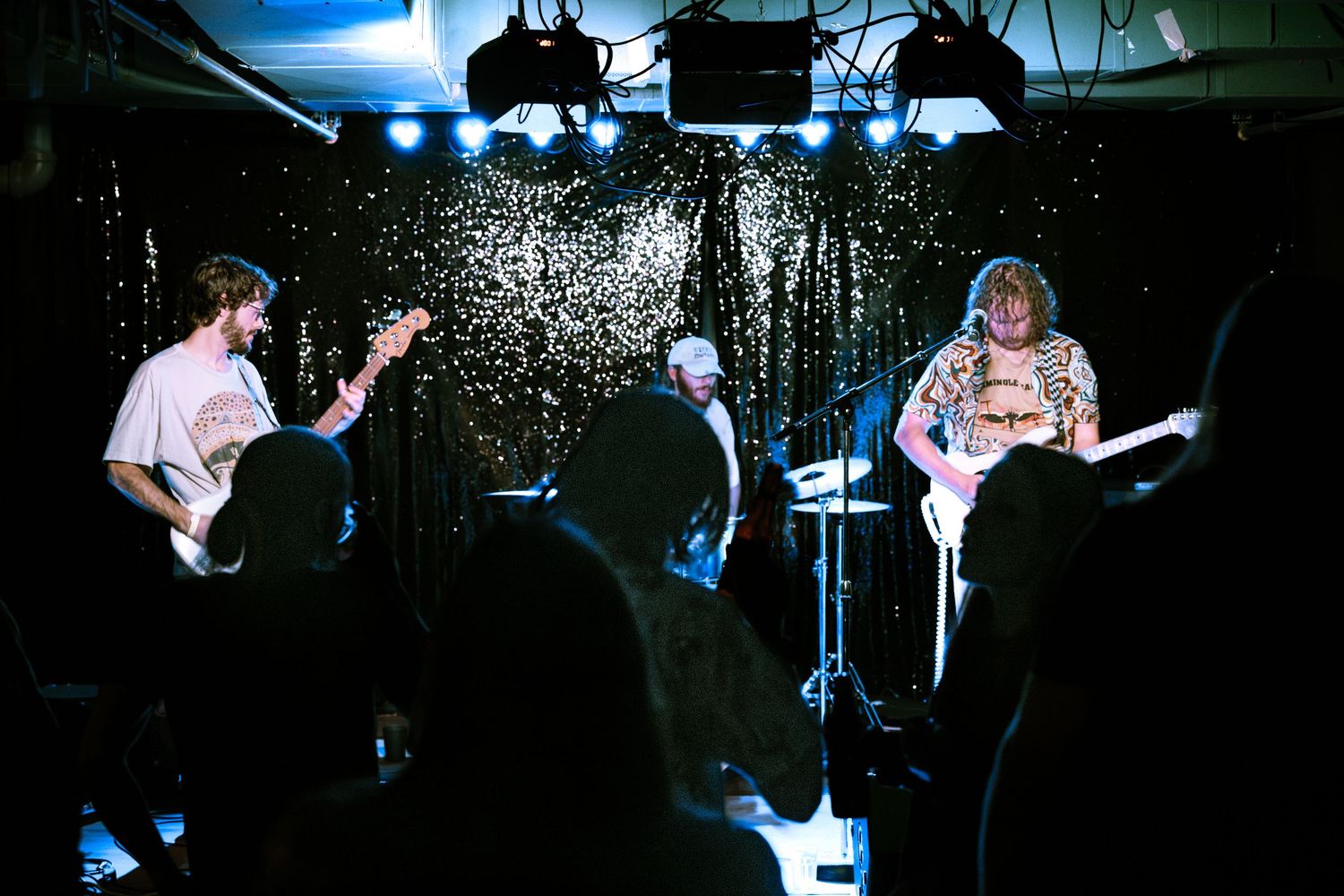 Three-piece band performing live on stage with glittery black backdrop.