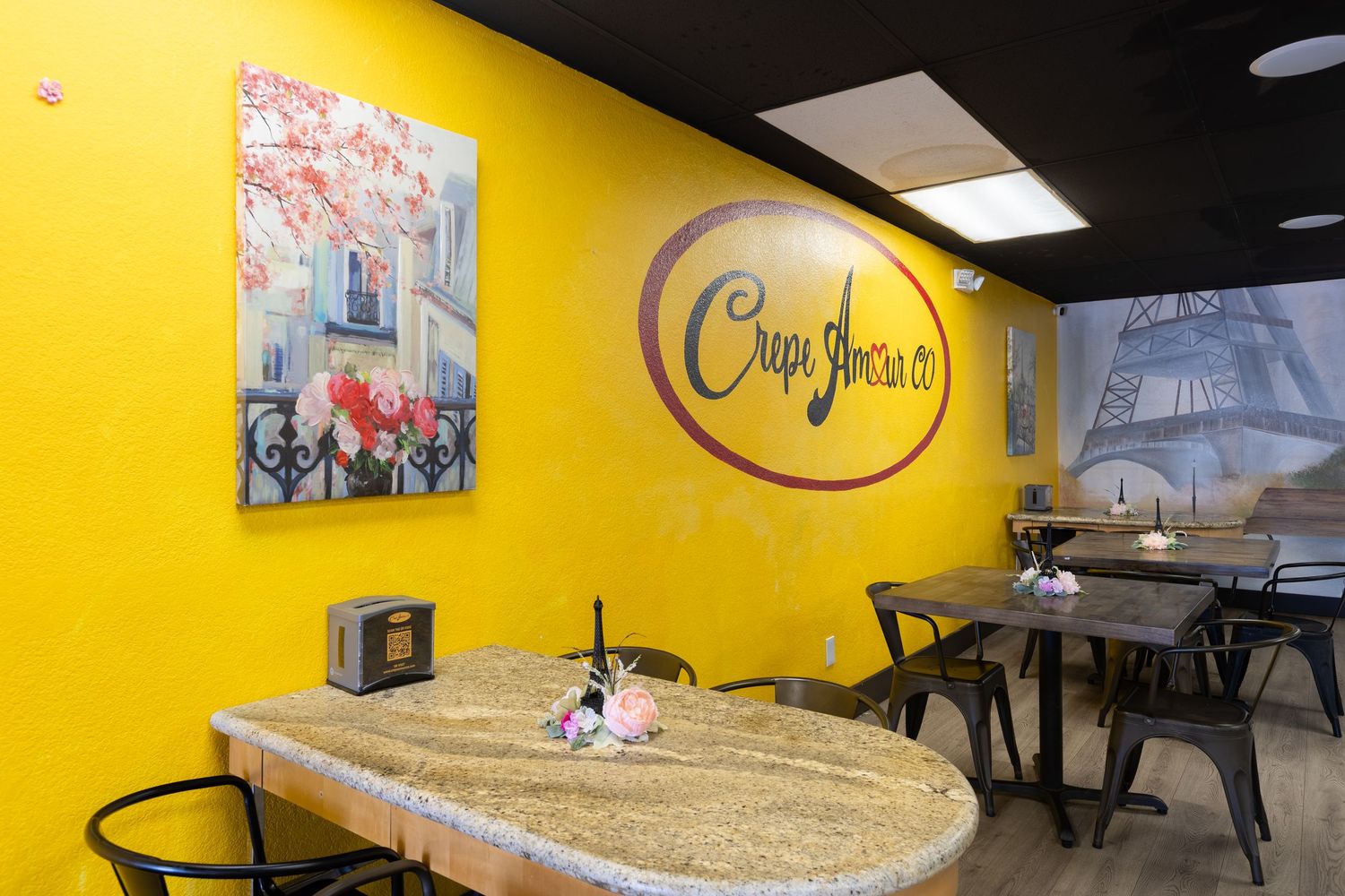 Crepe Jouvence restaurant interior with bold yellow walls, Eiffel Tower mural, and marble-top dining tables.