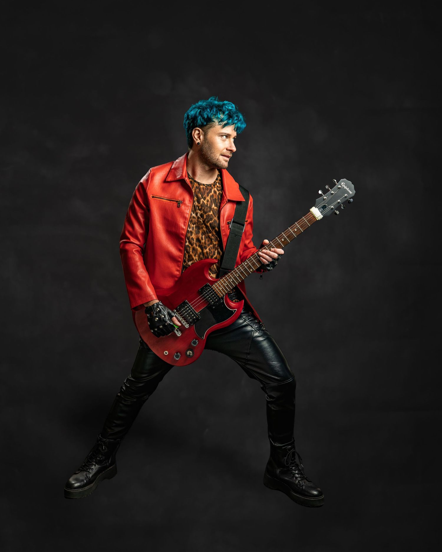 Teal-haired guitarist in red leather jacket plays electric guitar in dynamic rock pose on dark background.
