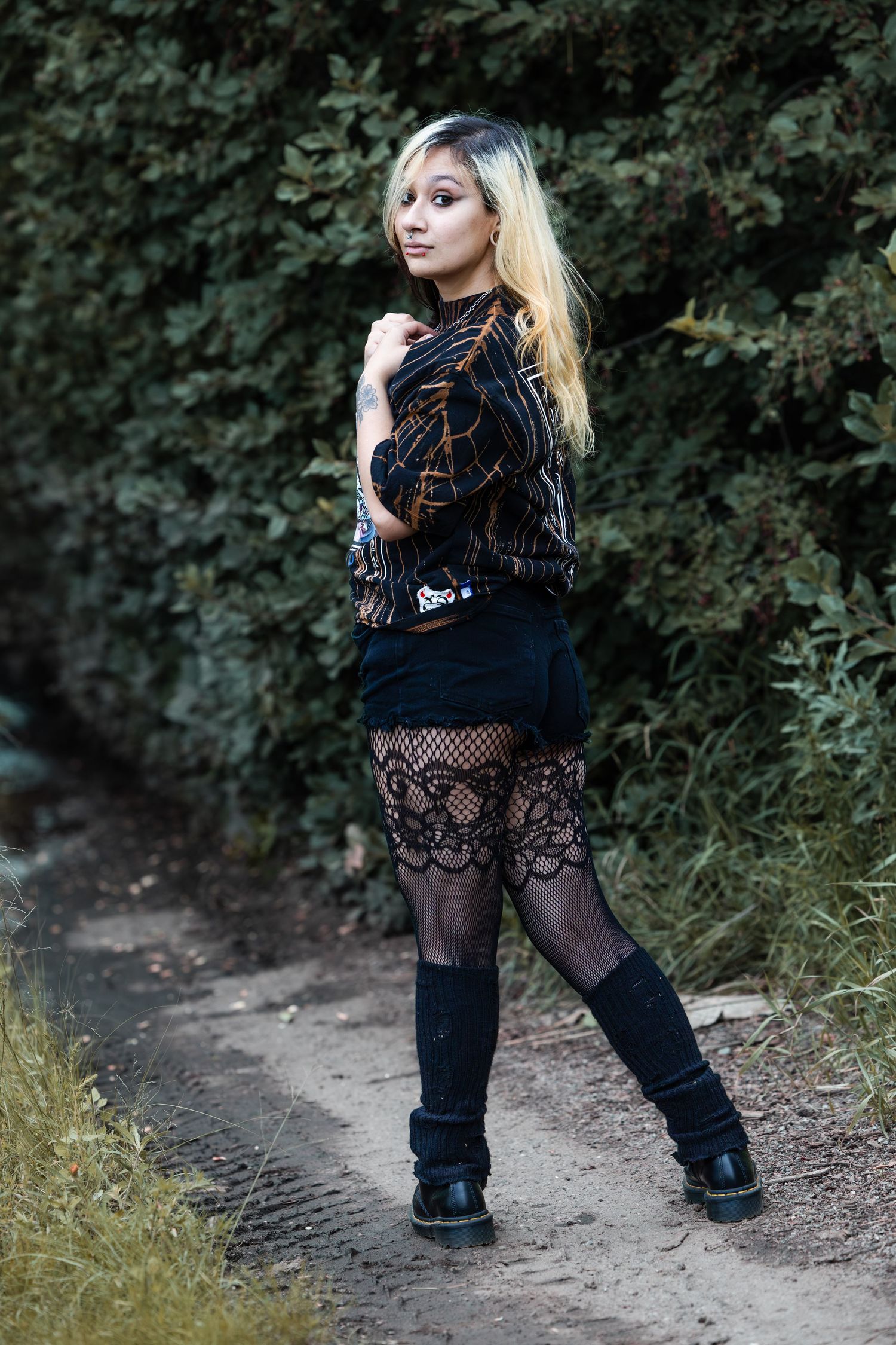 Fashion model in gothic style clothing poses on outdoor path with natural backdrop.