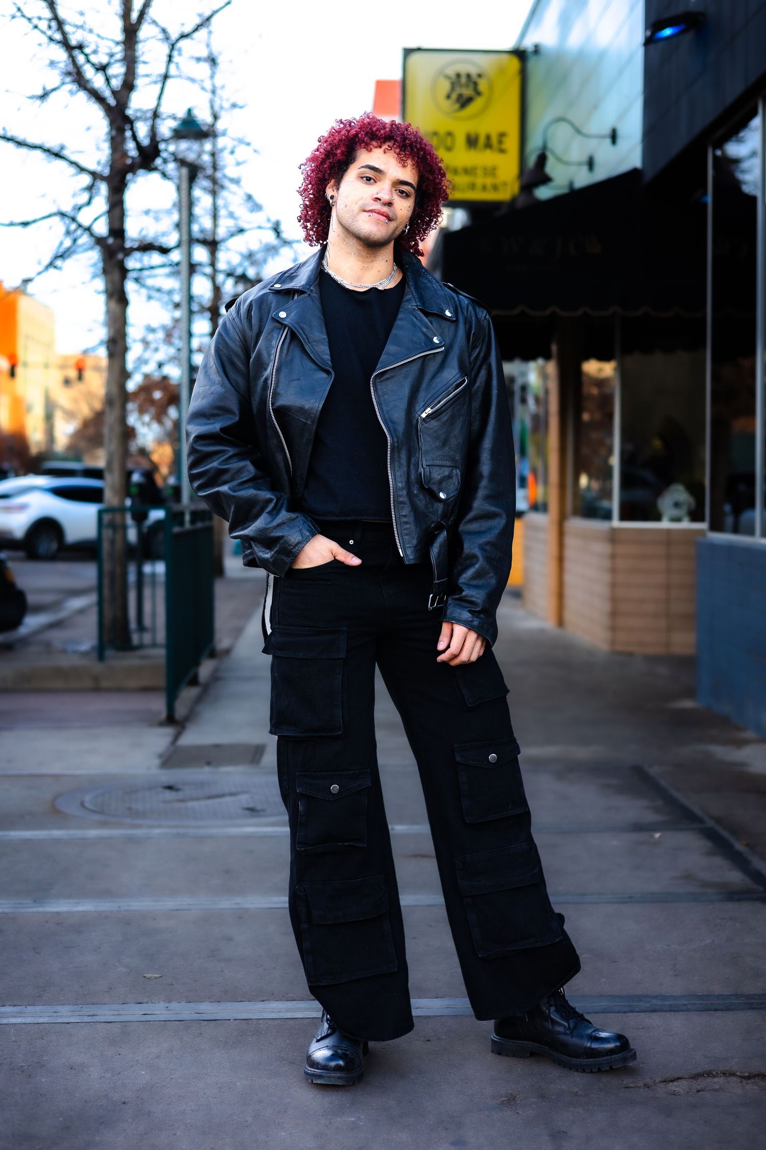 Street fashion look featuring bright magenta curls, leather jacket and cargo pants on urban sidewalk.