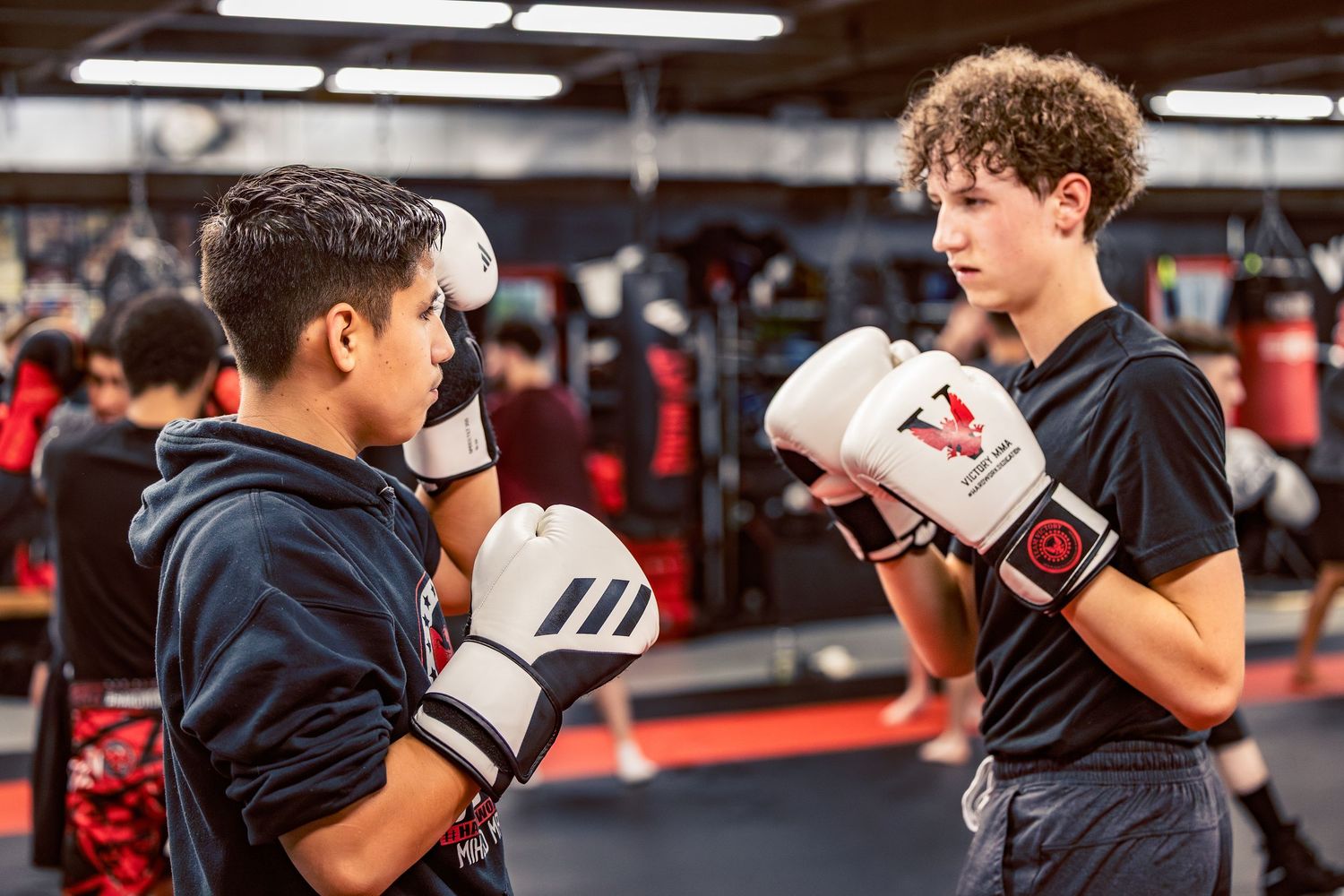 Boxing students practicing combinations under fluorescent gym lighting.