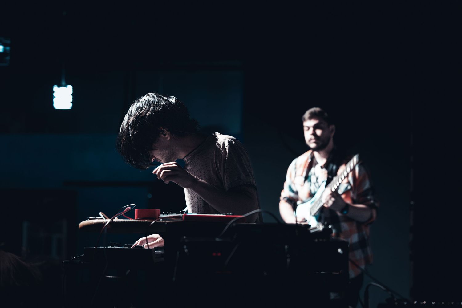 Musicians perform in a dimly lit concert venue with dramatic lighting effects.