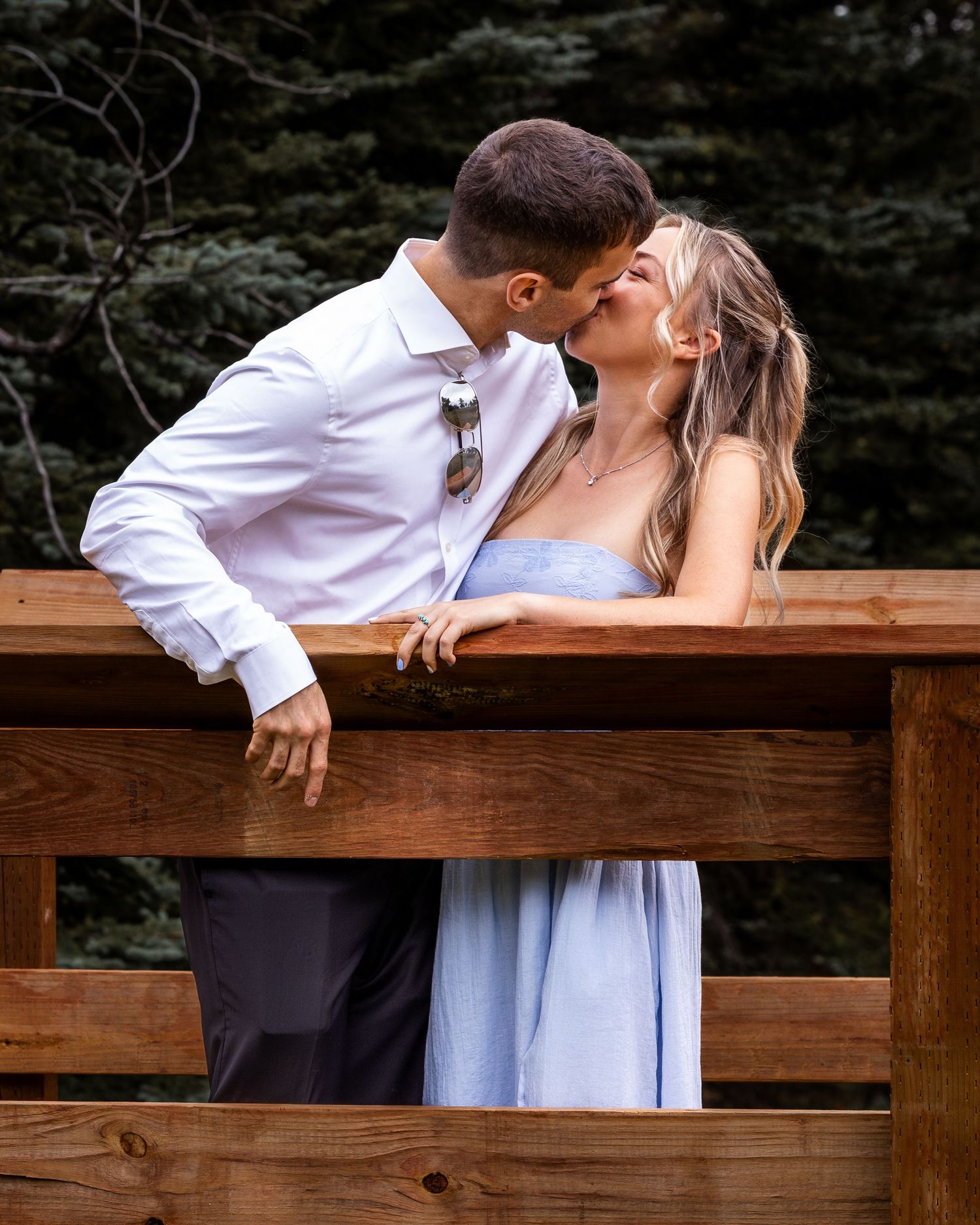 Couple sharing an intimate moment while leaning against a wooden deck railing.