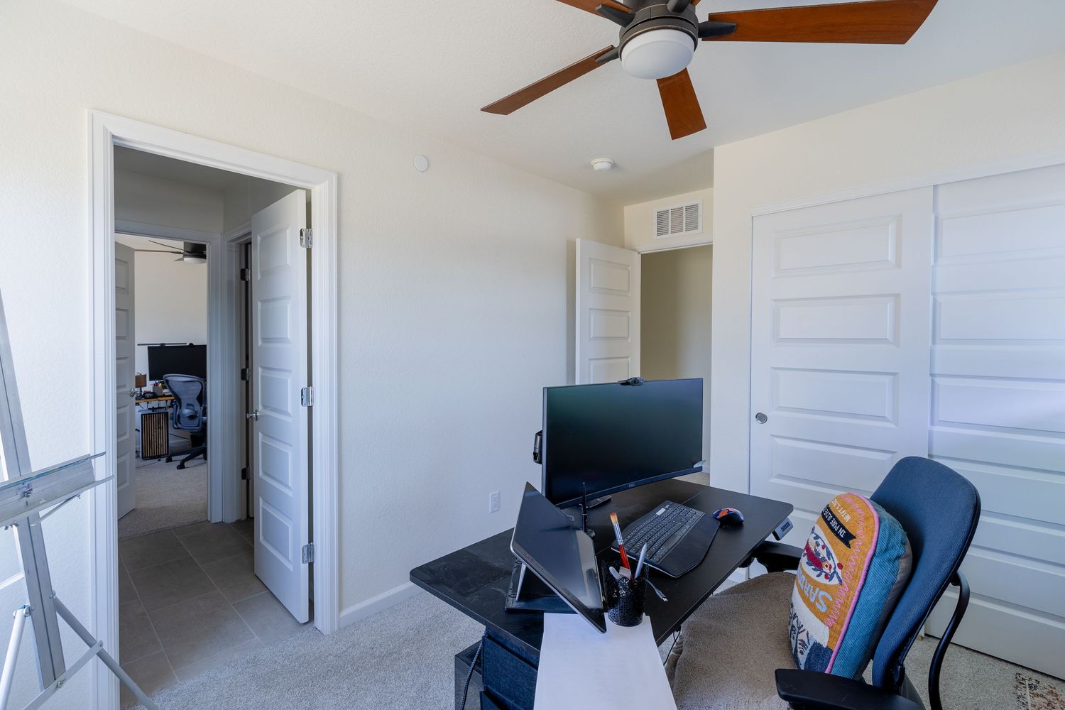 Home office with ceiling fan, desk, computer monitor, and closet with white bi-fold doors.