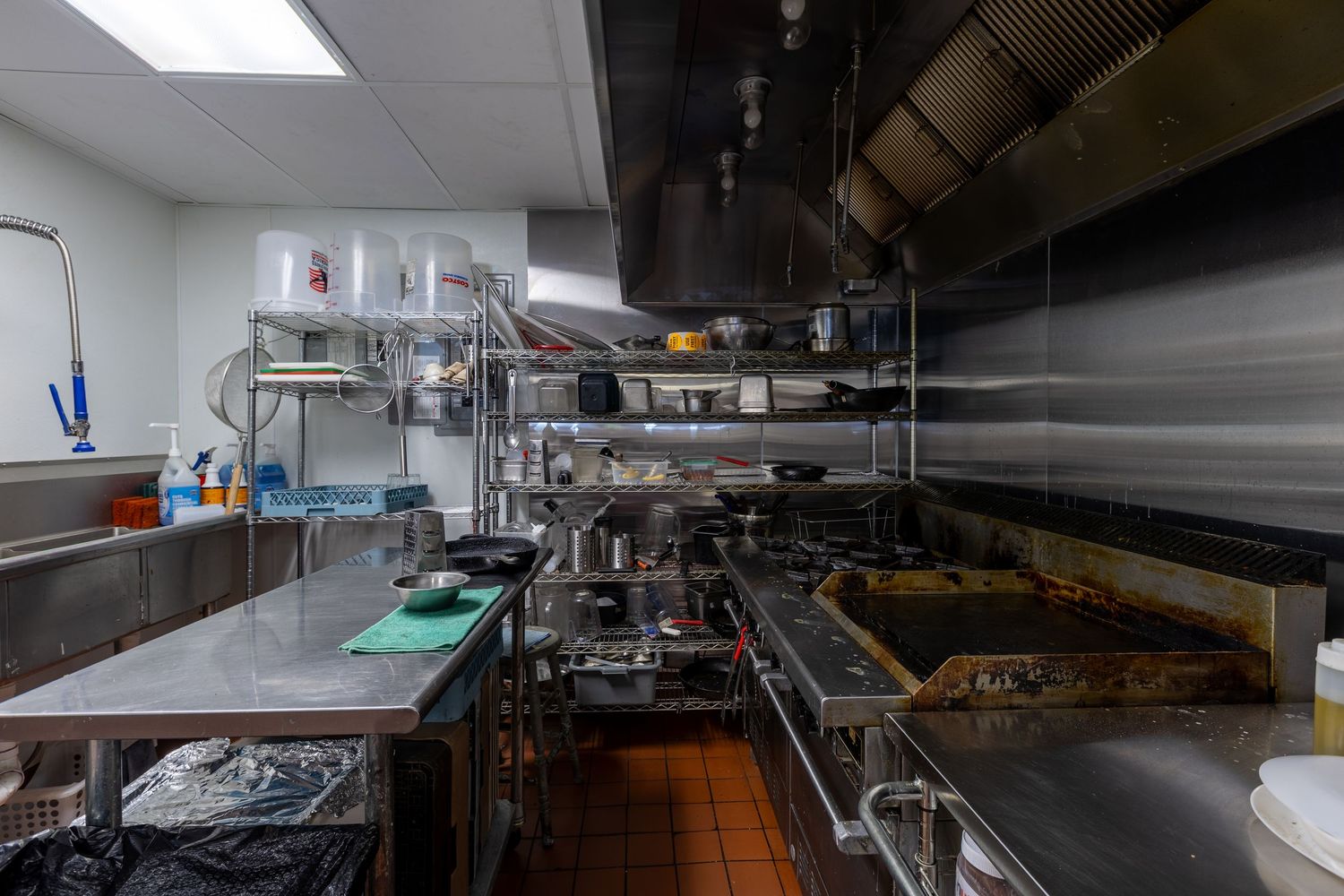 Stainless steel commercial kitchen with shelving, cooking equipment, and orange tile floors in a restaurant.