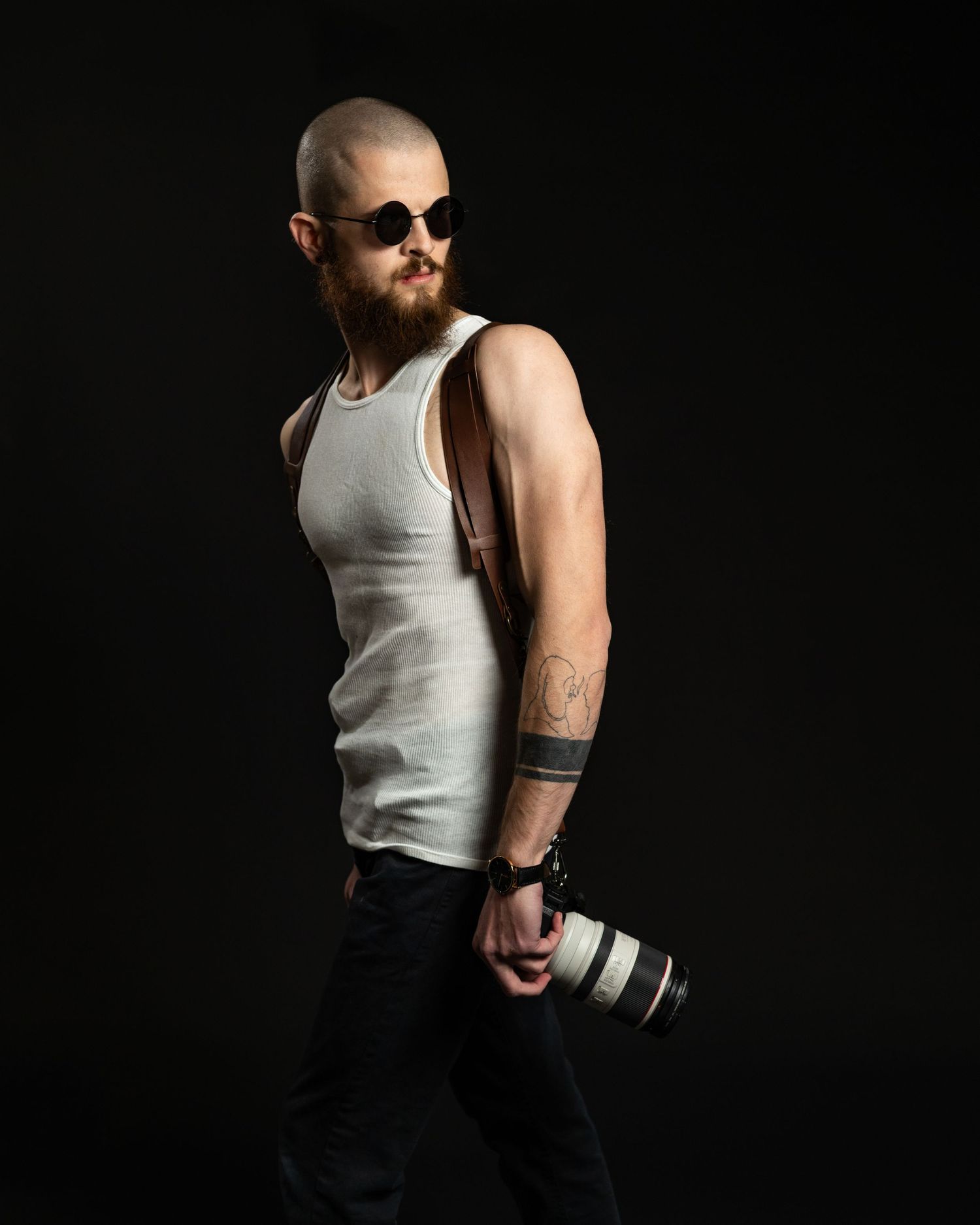 Side profile of photographer with camera and leather strap against black backdrop in dramatic lighting.