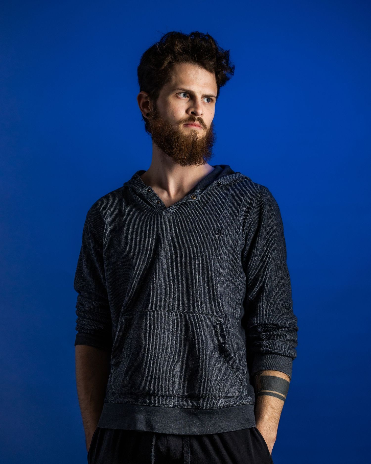 Man wearing a dark gray hoodie sweatshirt poses against a vibrant blue background.