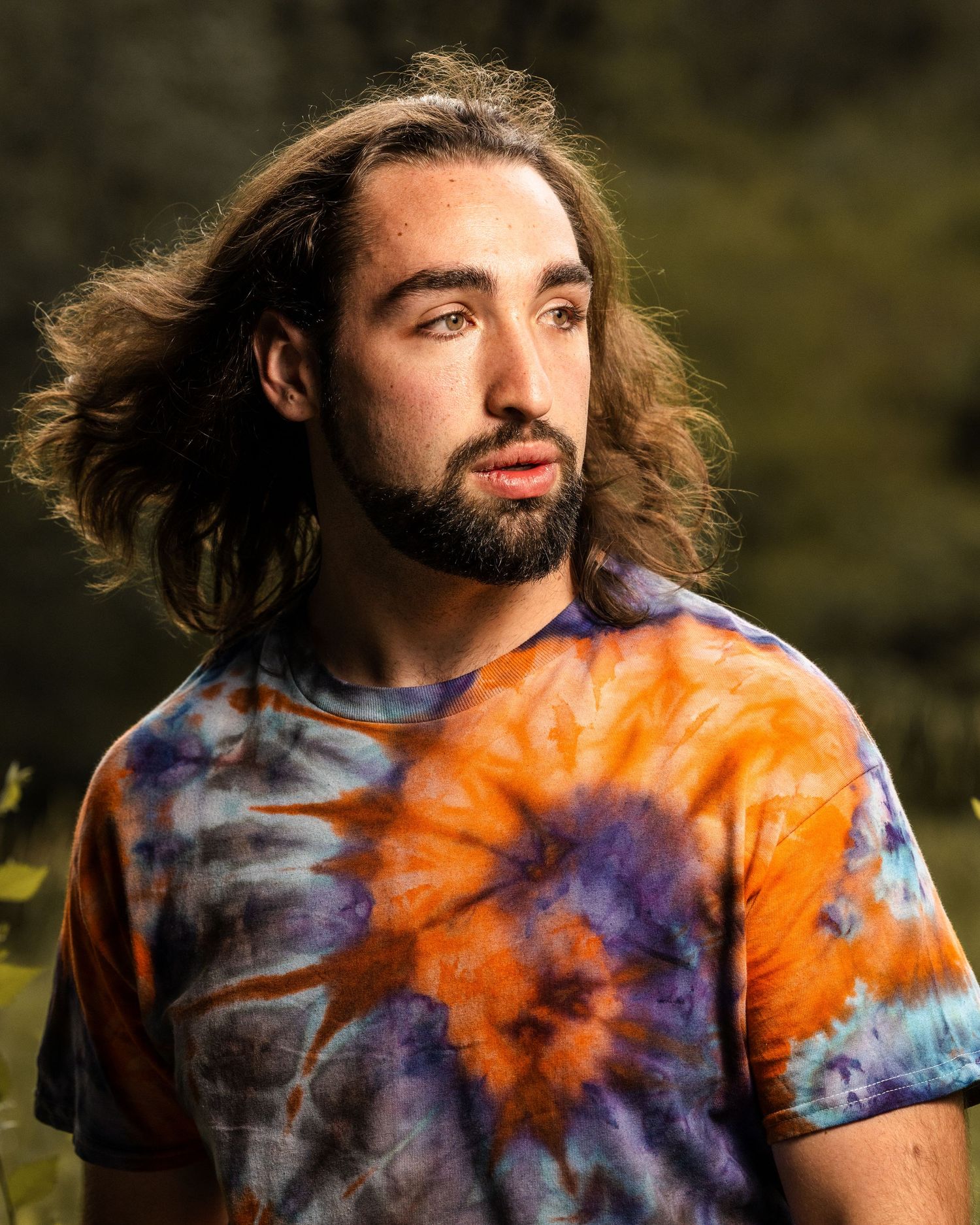 Artistic outdoor portrait featuring someone in an orange and purple tie-dye shirt with natural backlighting.