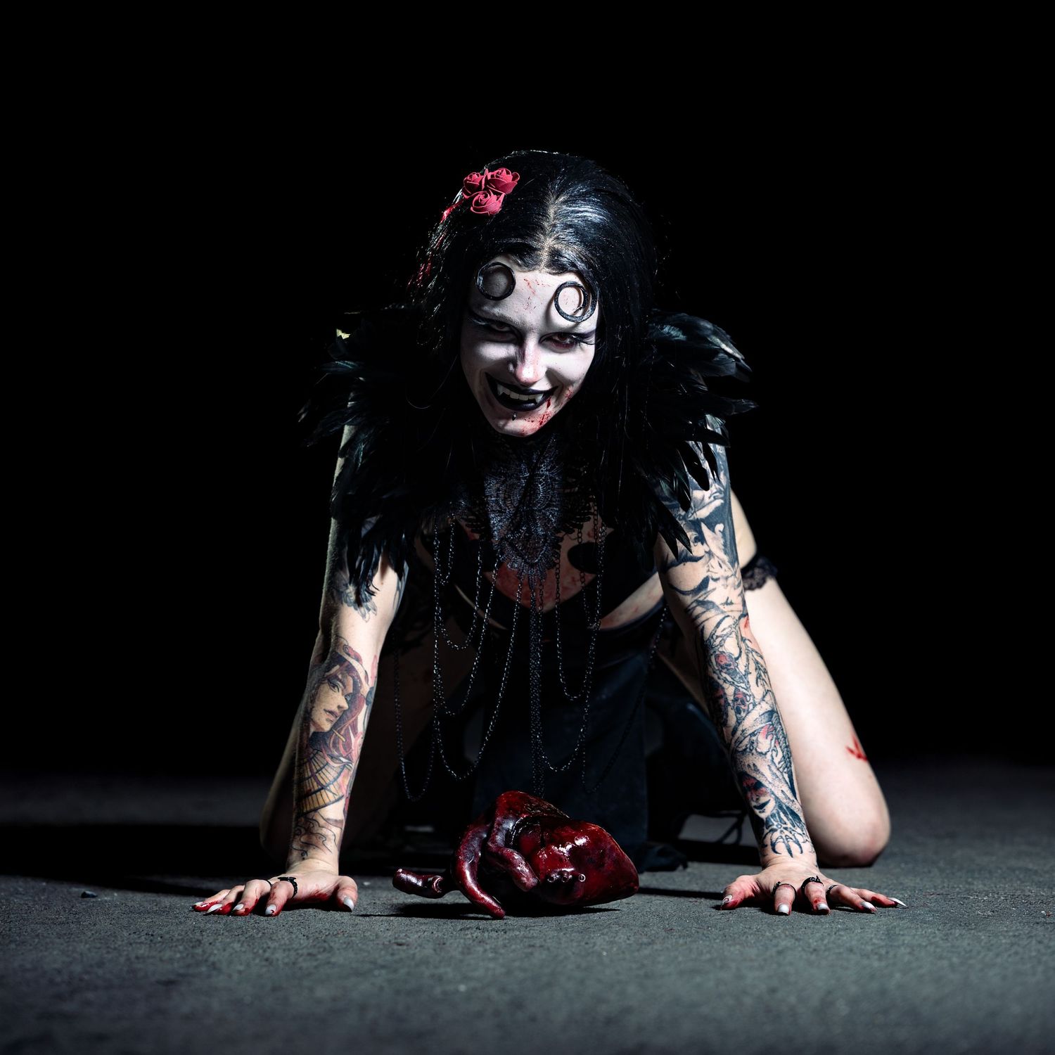 Tattooed woman in dark gothic angel costume with spiral eye makeup crawling on floor with bloody heart.