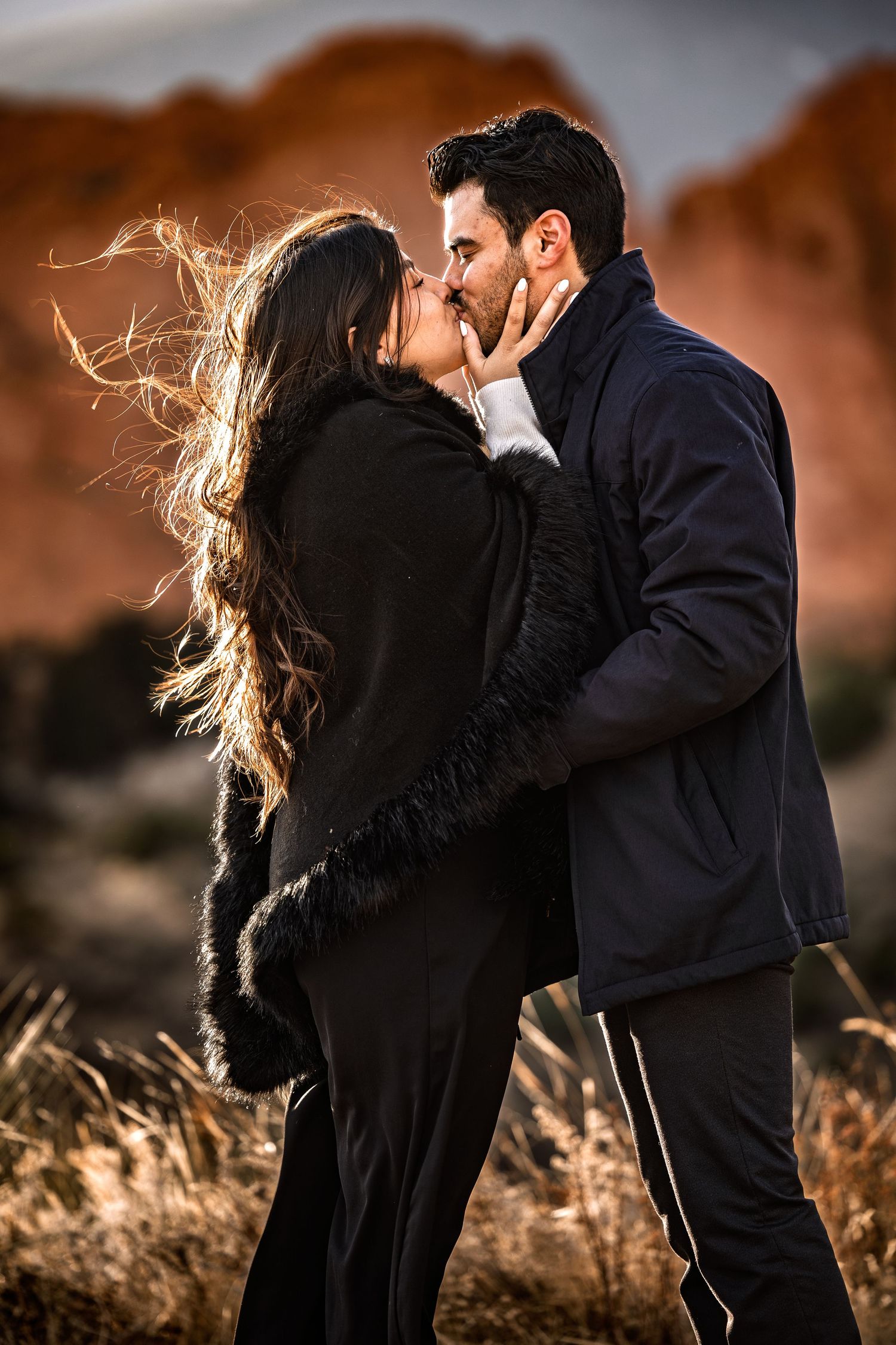 Romantic couple sharing an intimate moment at sunset with windswept hair against red rock formations in the background.
