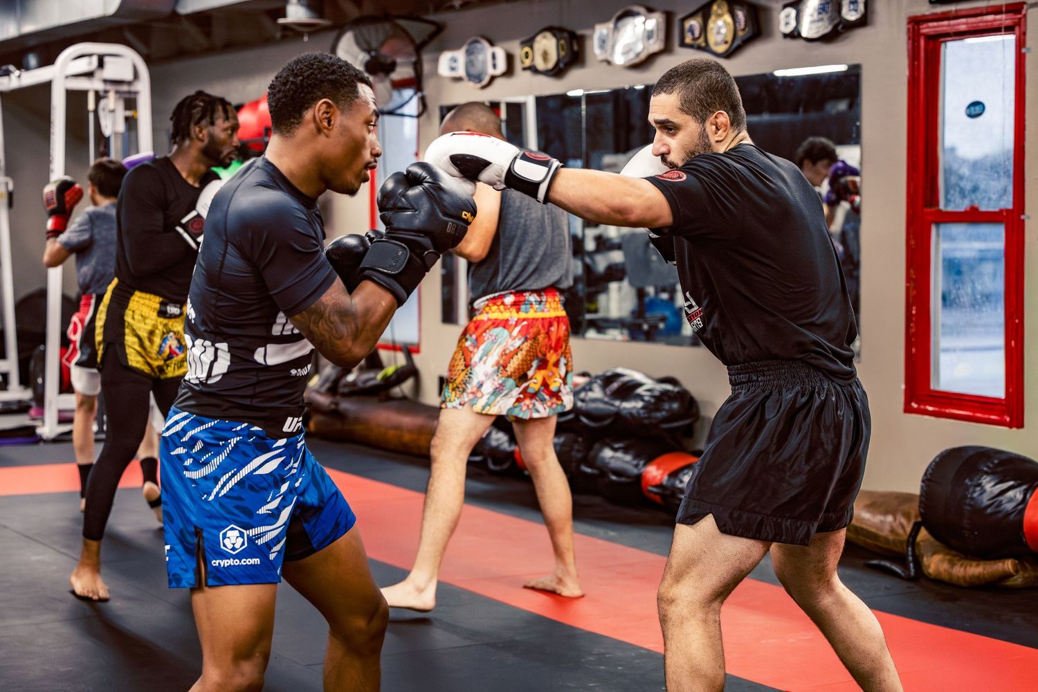 Martial artists training together on red mats in a gym decorated with championship belts.