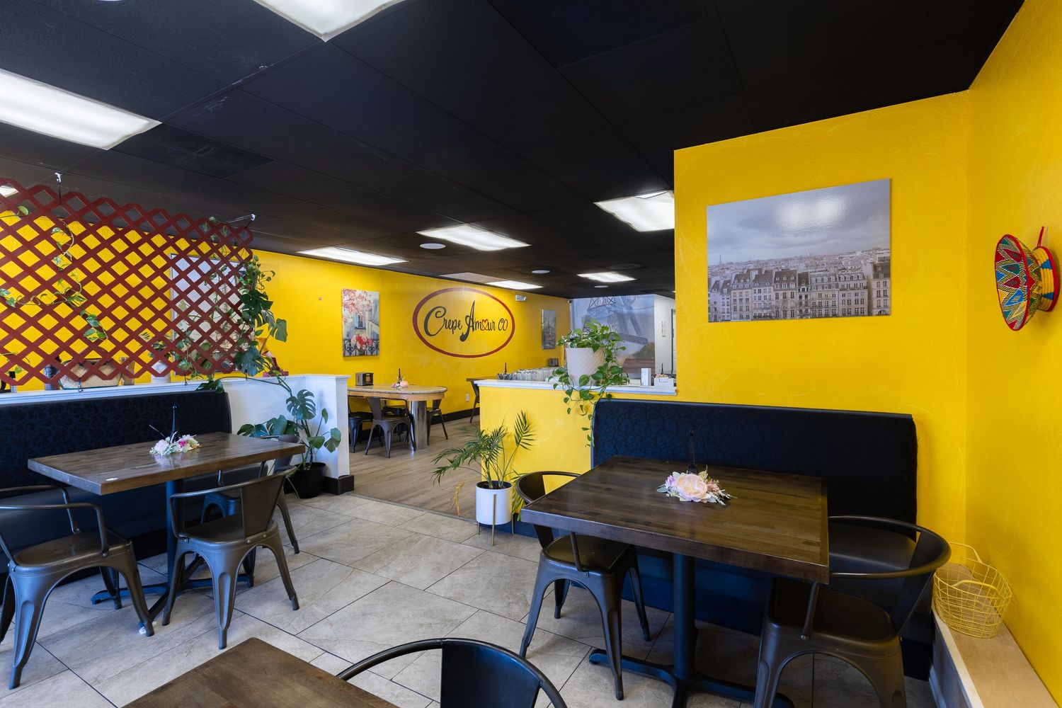 Bright yellow walls and black ceiling accent a cozy cafe dining area with wooden tables and metal chairs.