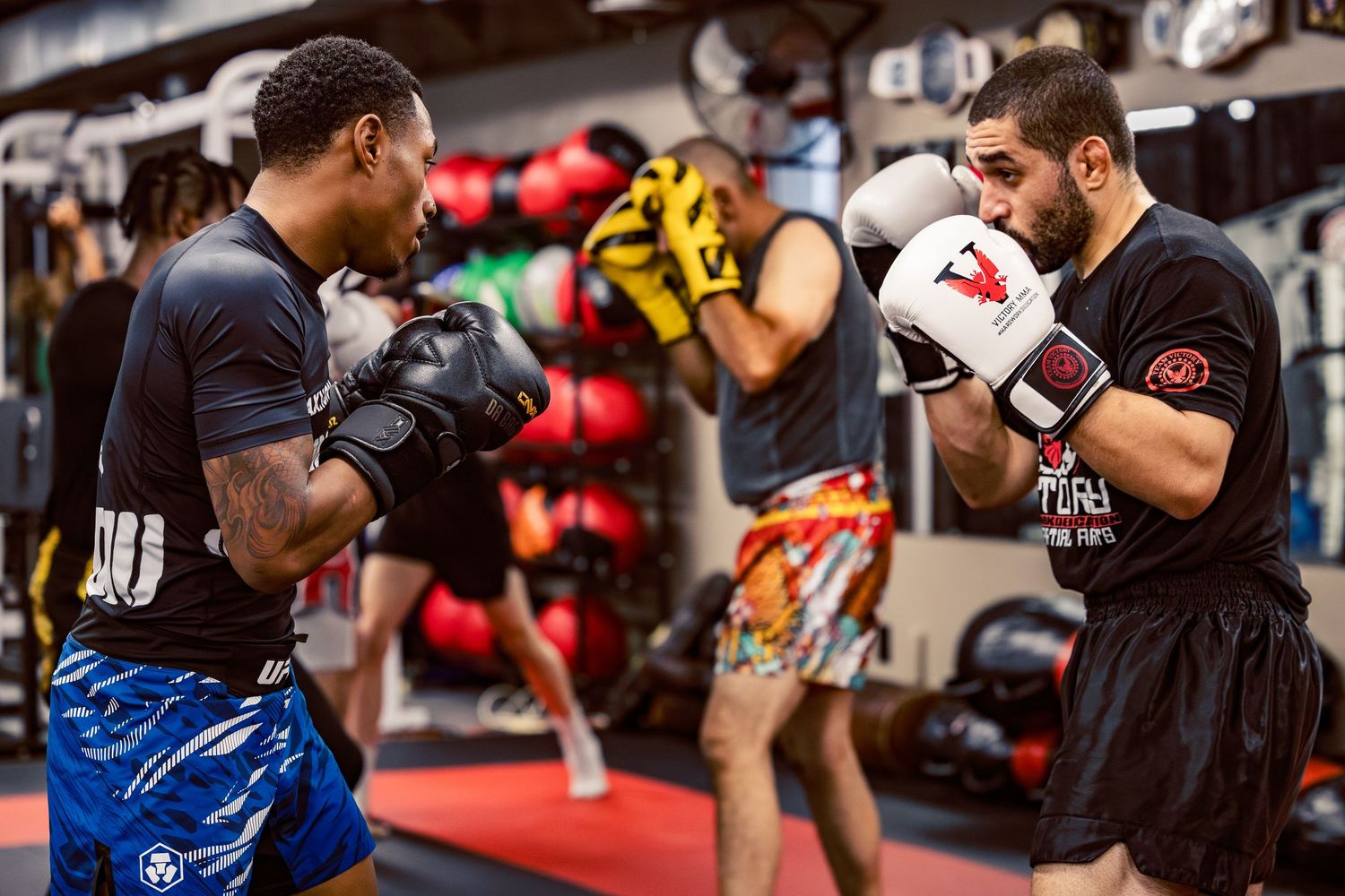 Athletes training in a kickboxing gym with championship belts displayed on the wall behind them.