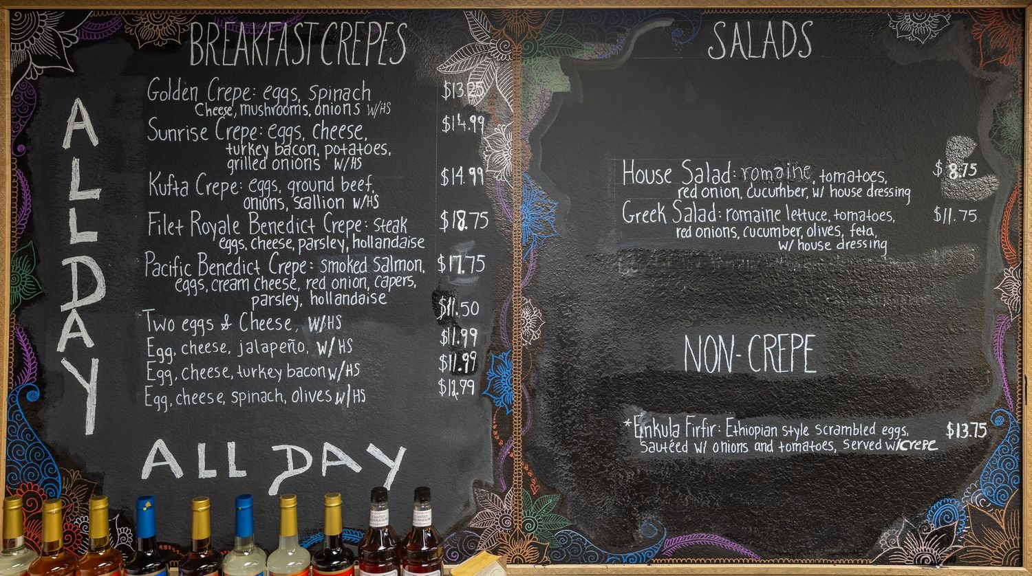 Chalkboard menu displaying breakfast crepes, salads, and non-crepe options with pricing at a casual cafe.