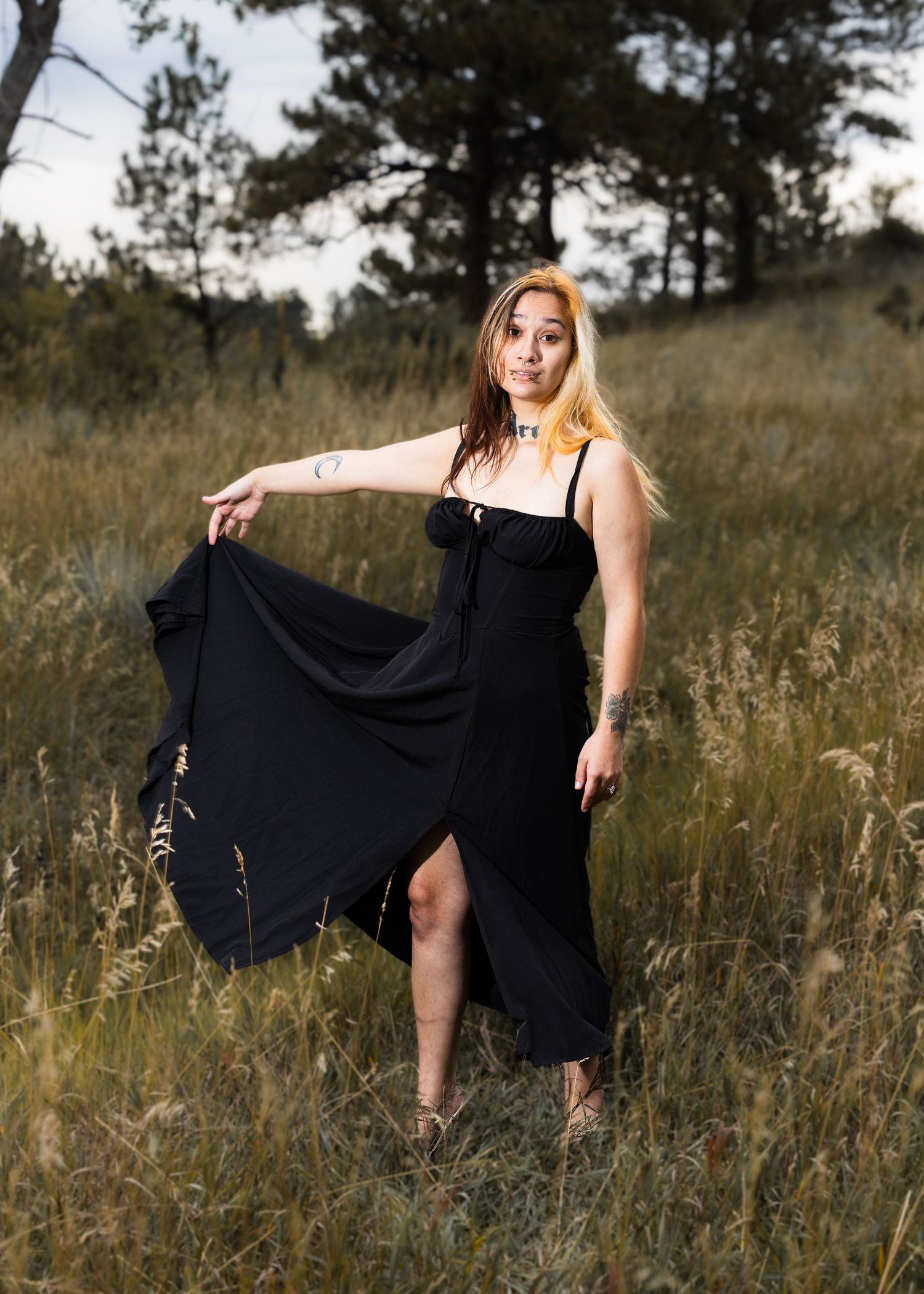 Woman in flowing black dress twirls playfully in sunlit meadow.