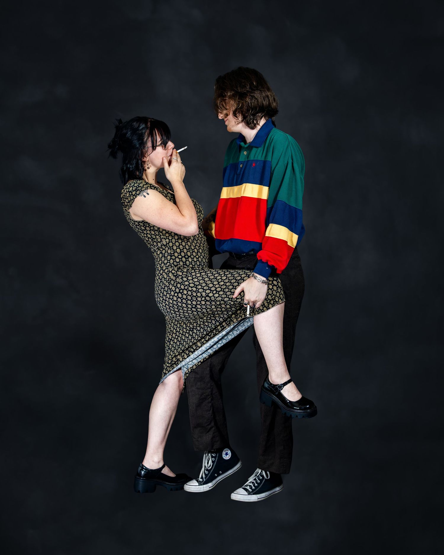 Two young people in retro outfits dancing together against a dark studio background.
