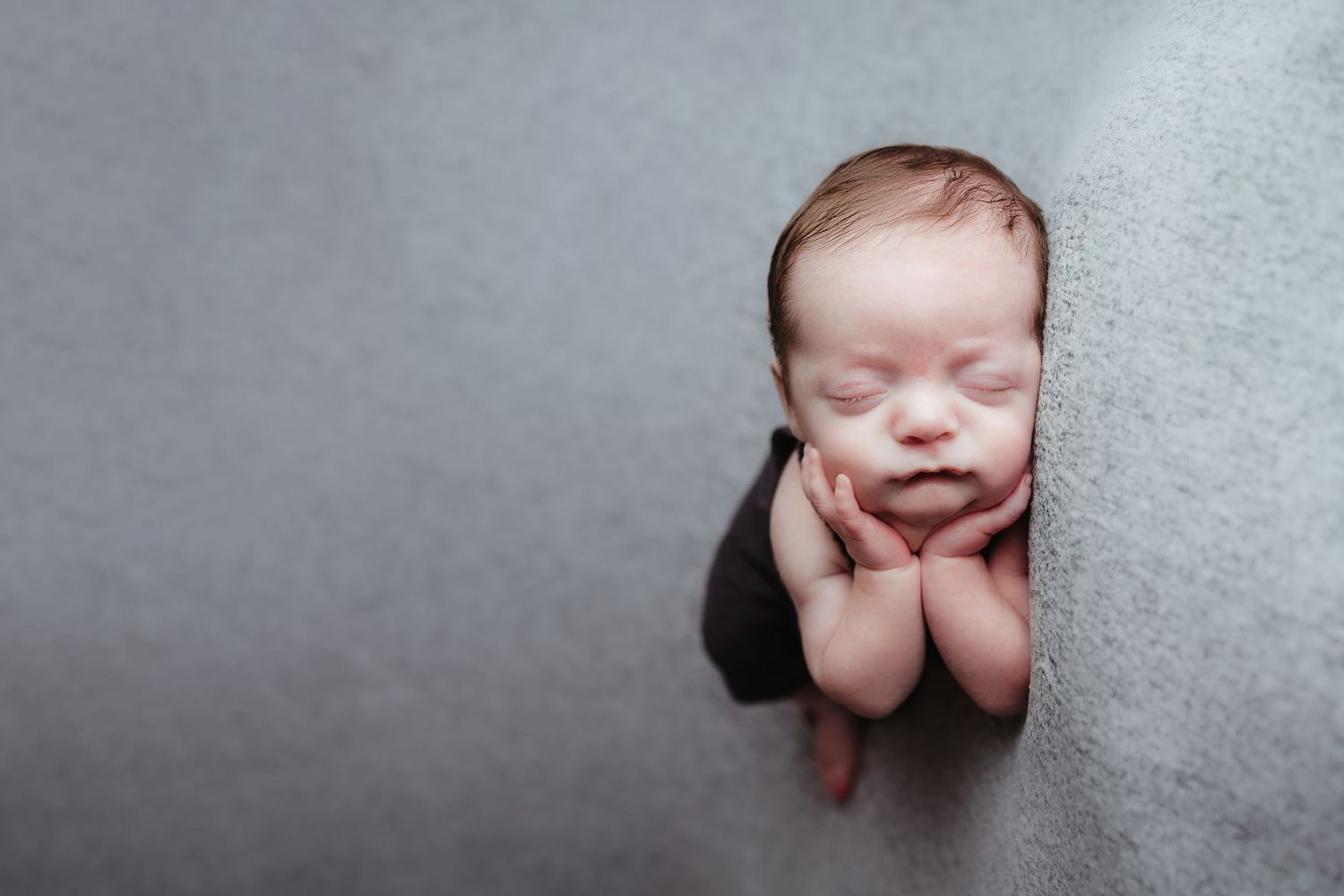 Sleeping newborn baby tucked in gray blanket with hands under chin in cozy wrap pose.