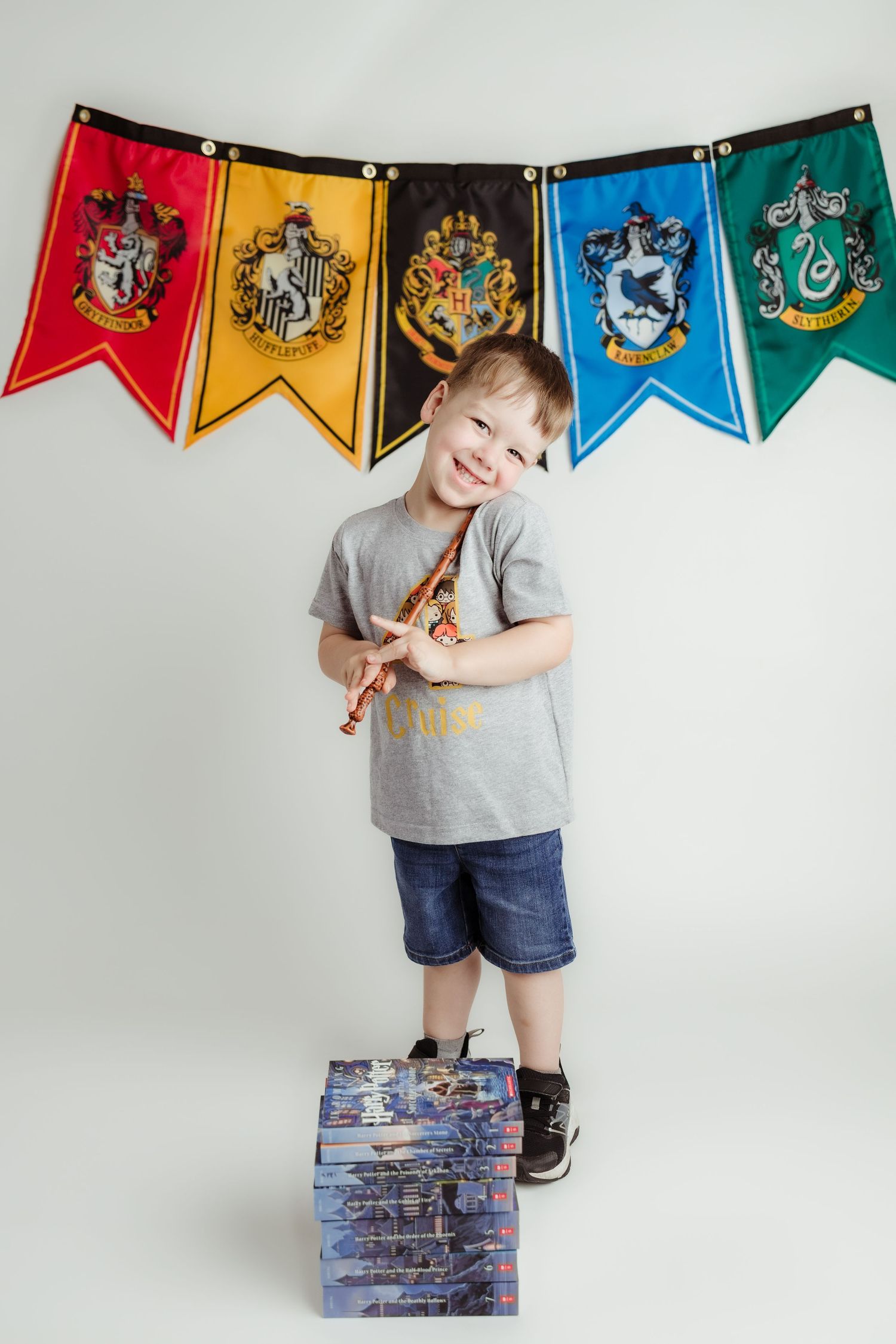 Smiling boy holding wand with Harry Potter house banners background at birthday party.