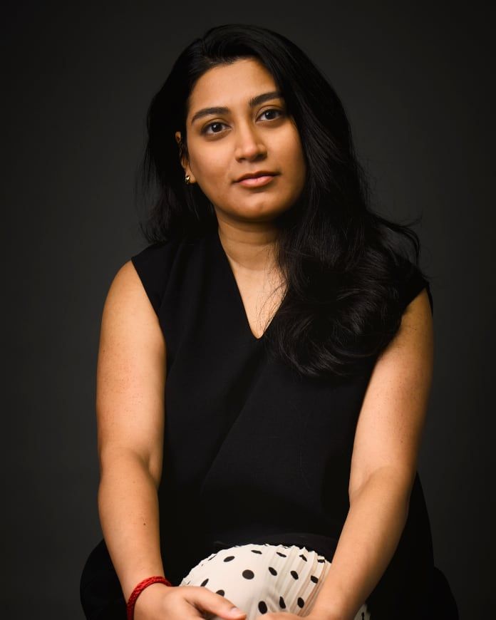 Young woman in black sleeveless top holding polka dot fabric poses for studio portrait on dark background.