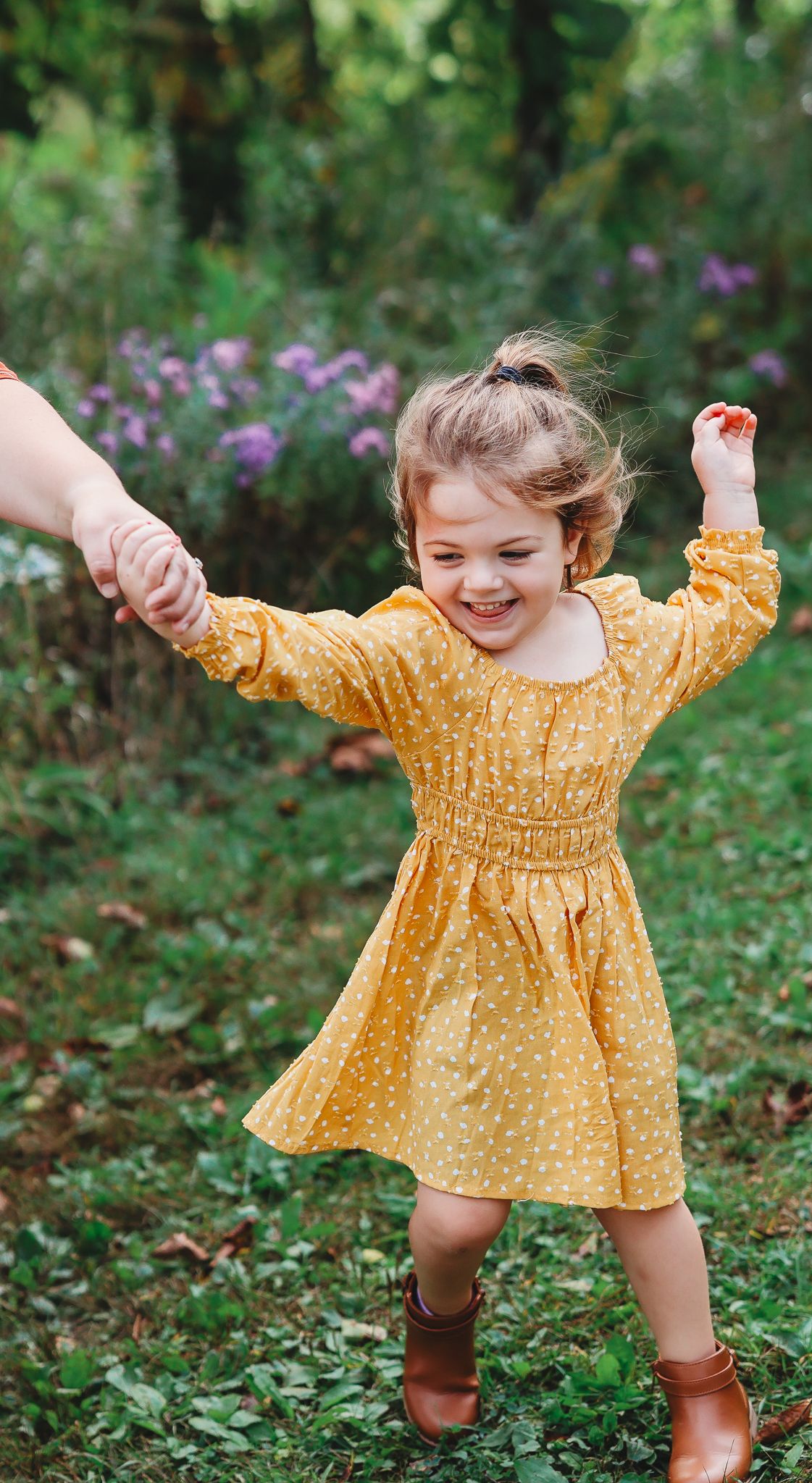 Cheerful little girl in yellow polka dot dress dancing and holding hands in a garden.