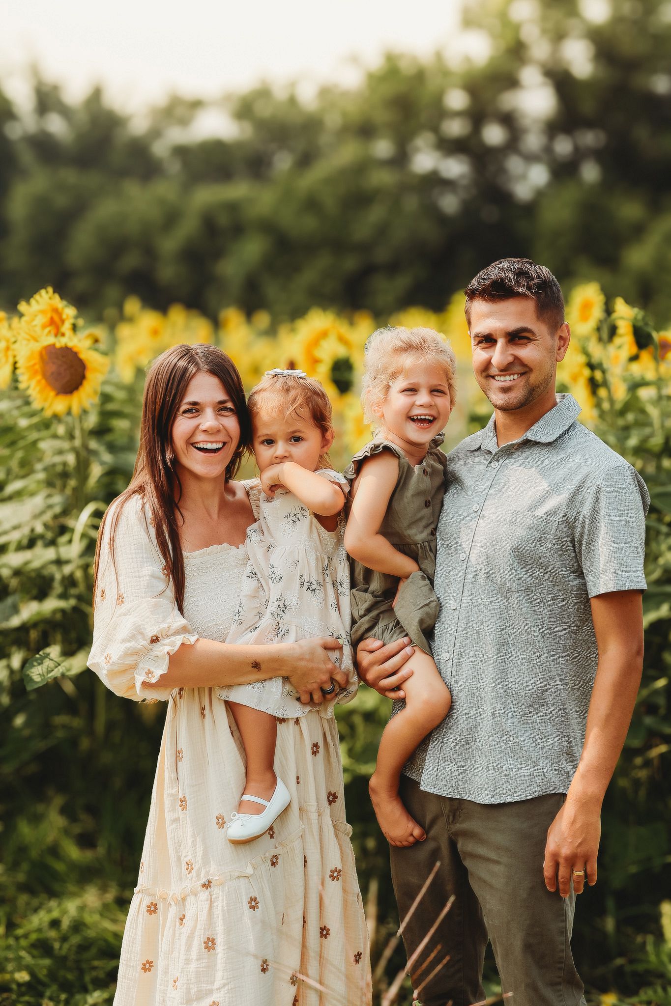 Happy family of four smiling together in a golden sunflower field at sunset.