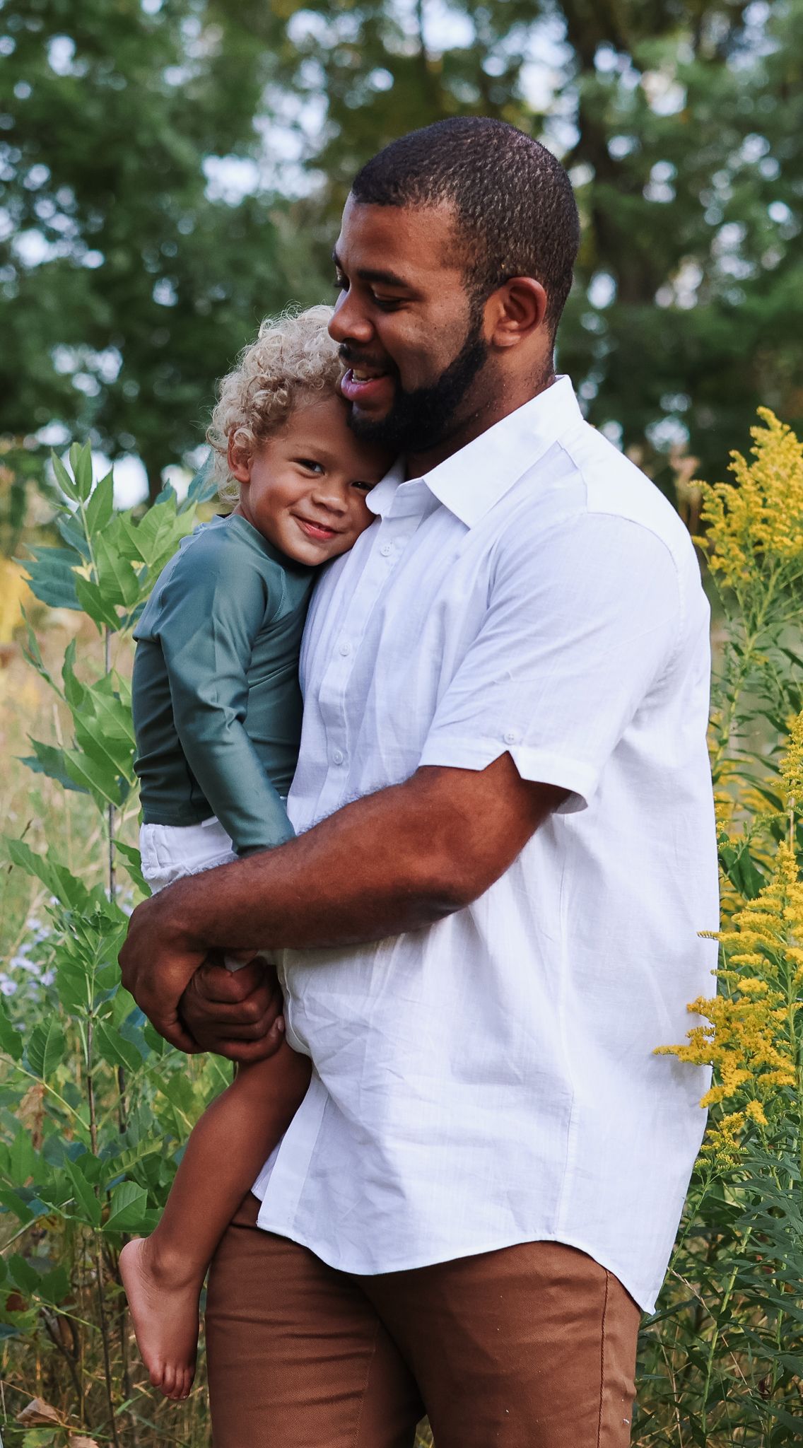 Father holding curly-haired child in green shirt in garden.