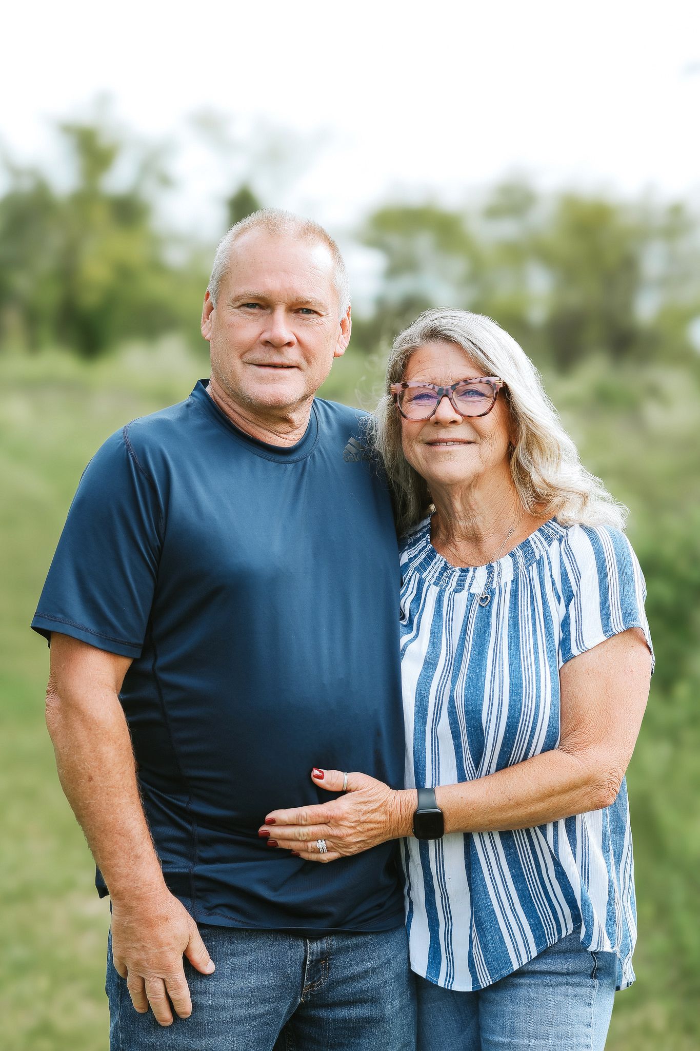 Older couple smiling together outdoors in a green field, woman in striped blouse.