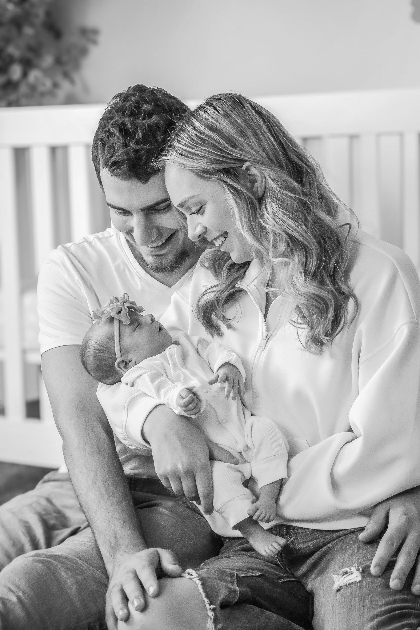 Black and white photo of happy parents smiling at their newborn baby in a nursery.