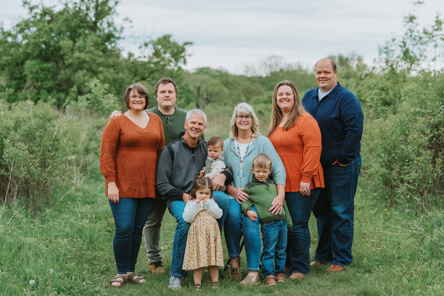 Extended multigenerational family posing together in lush green meadow during outdoor portrait session.