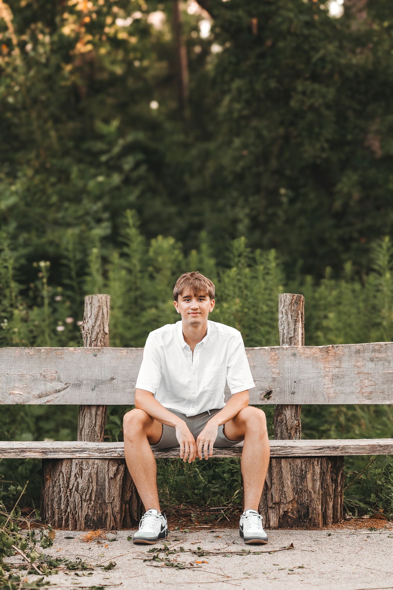 Young man in white shirt and shorts sitting on a rustic wooden bench in a park setting.