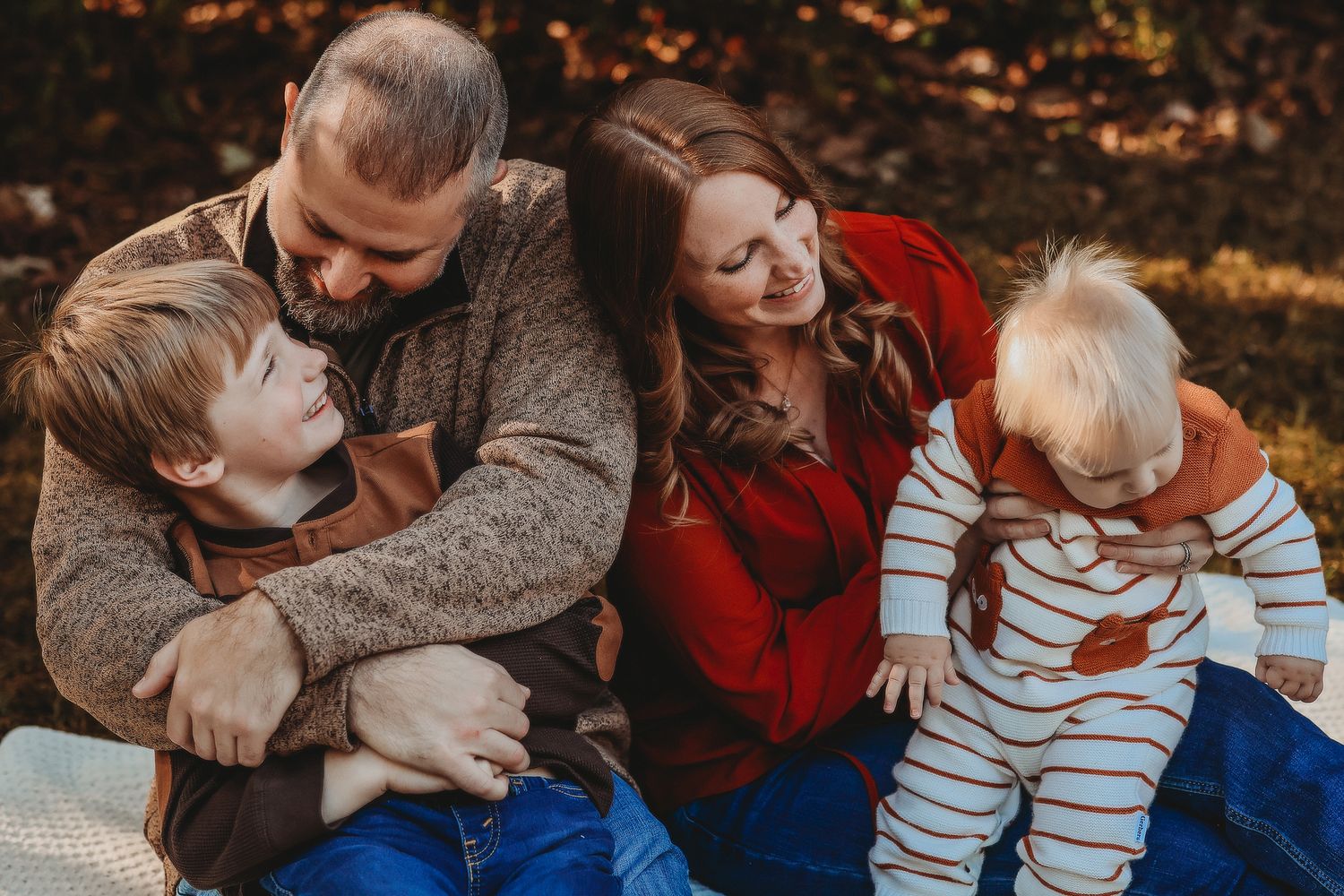 Family of four sharing a joyful moment on a blanket surrounded by golden autumn leaves.