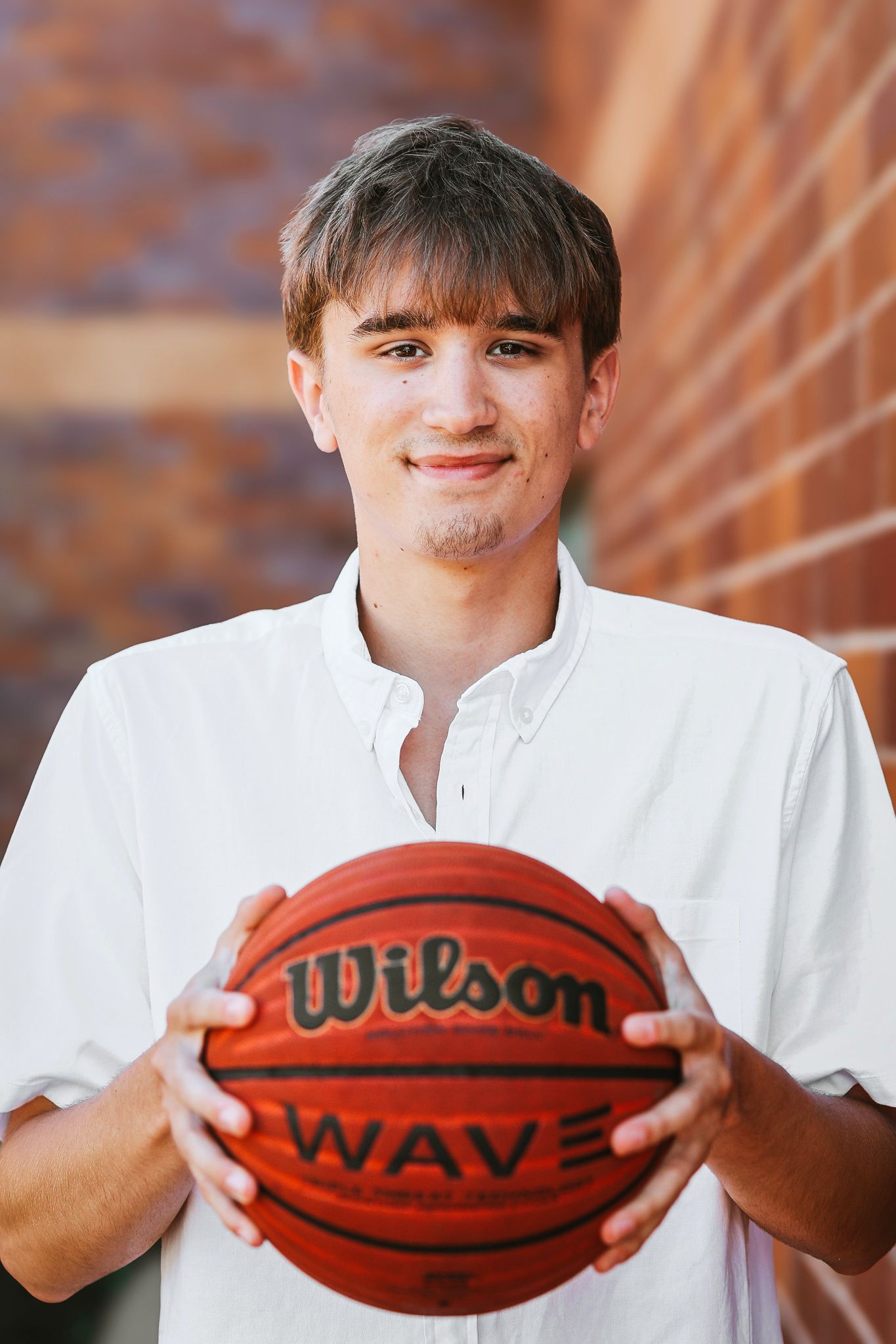 Young man in white shirt holding a Wilson Wave basketball against a brick wall background.
