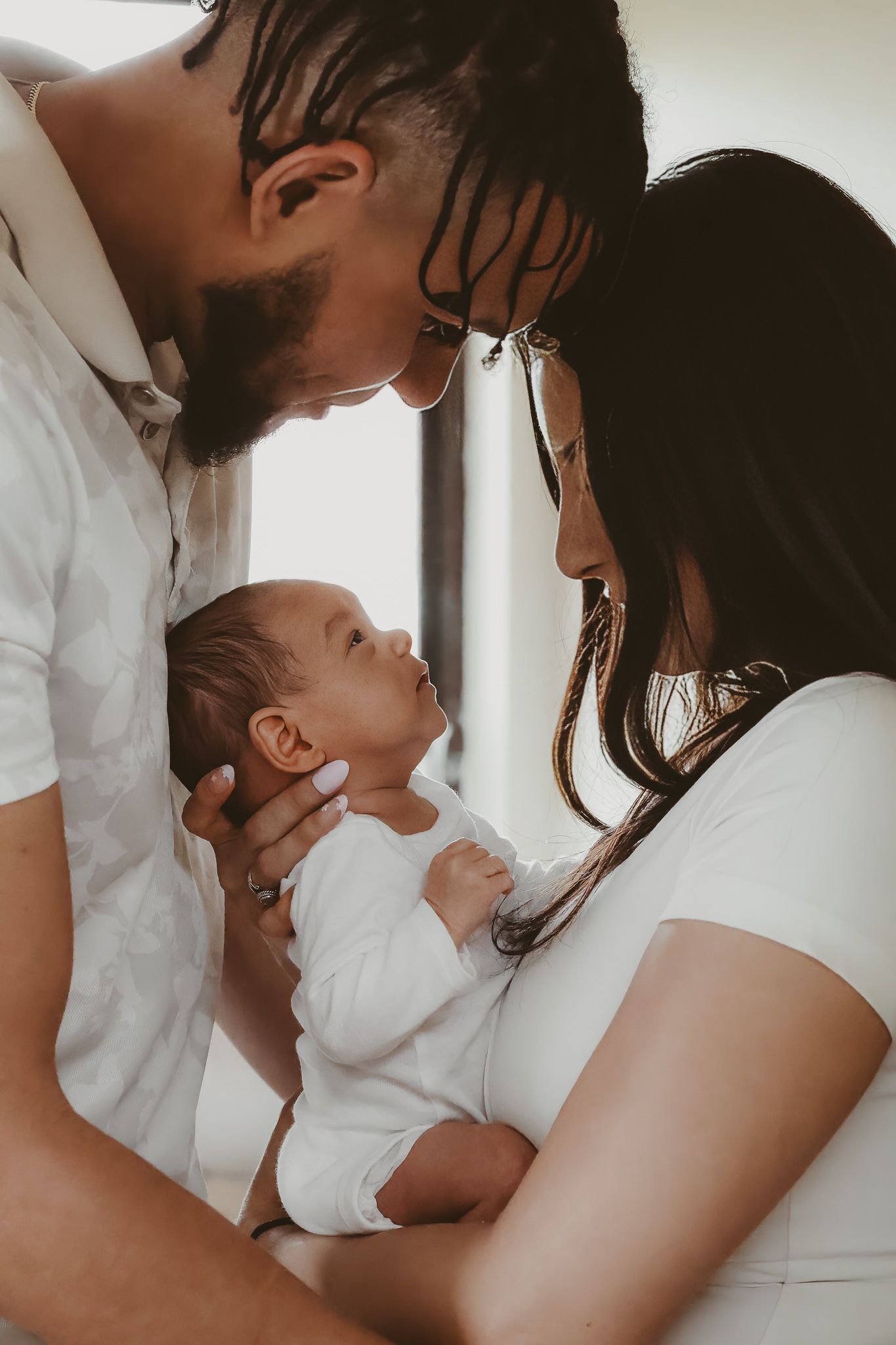 Tender moment as new parents gaze lovingly at newborn baby in bright indoor setting.
