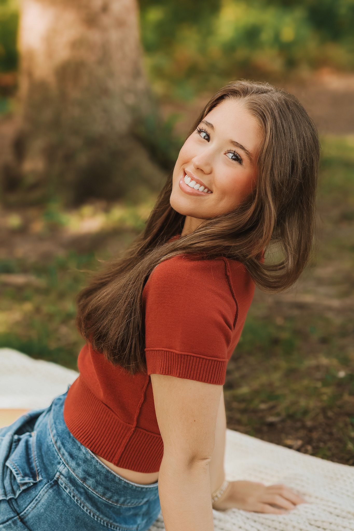 Teenage girl in rust red top and denim skirt smiling during outdoor senior portrait session.