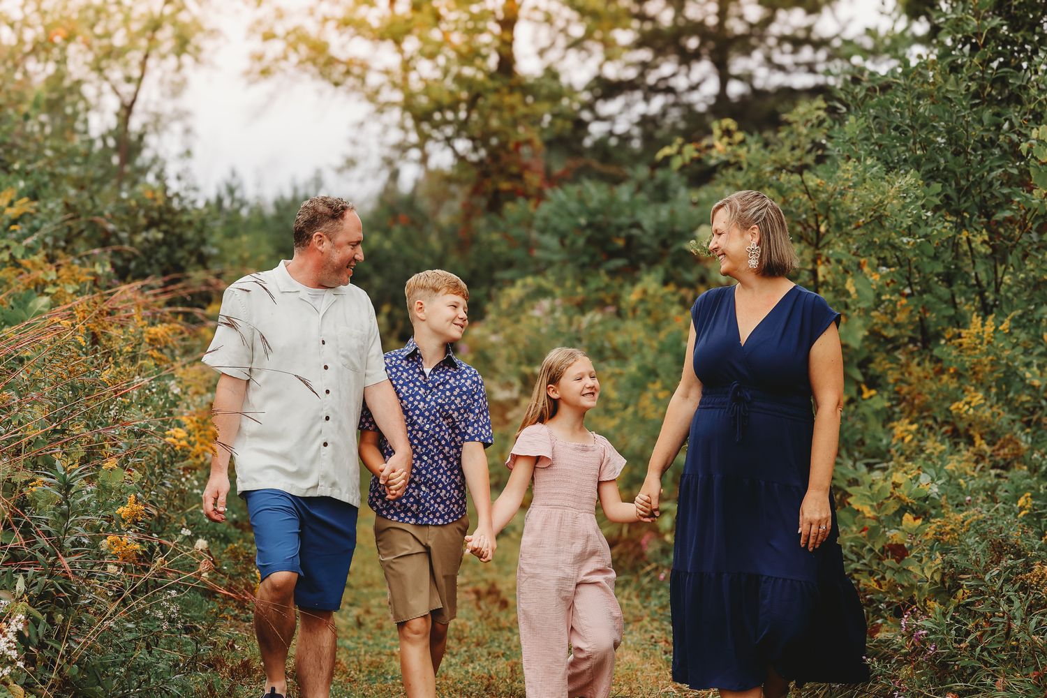 Happy family of four walking hand in hand through a sunny outdoor field.
