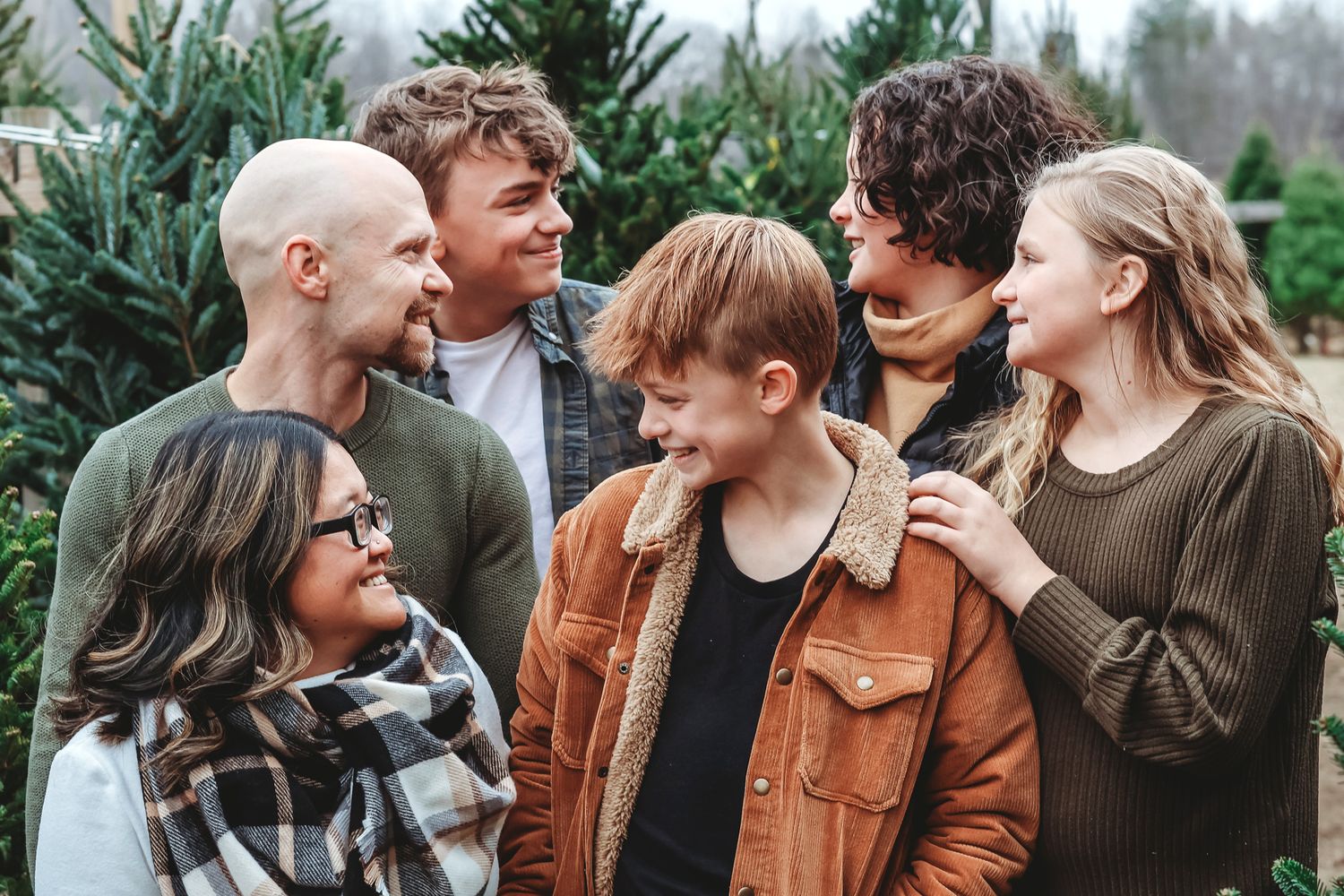 A blended family of six laughs and smiles together at a lush Christmas tree farm.