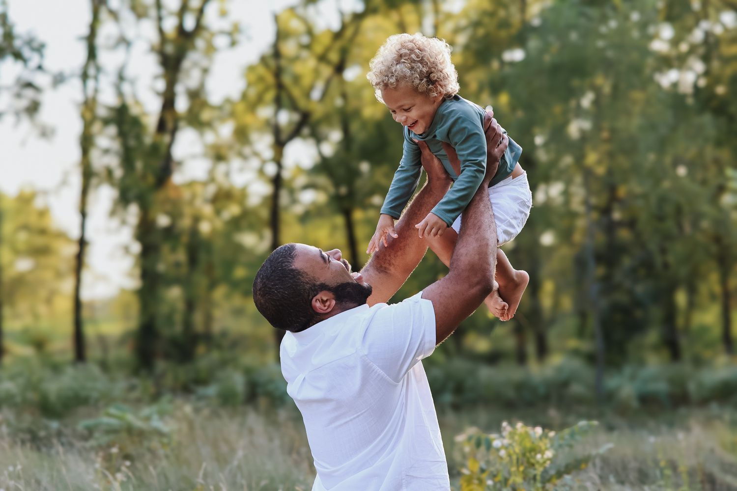 Father lifting laughing toddler in the air in nature.