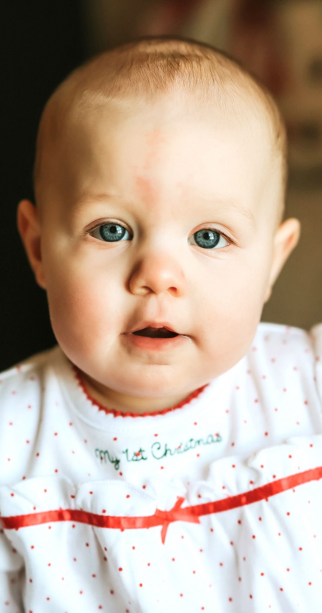 Close-up portrait of a blue-eyed baby in a My 1st Christmas white and red outfit.