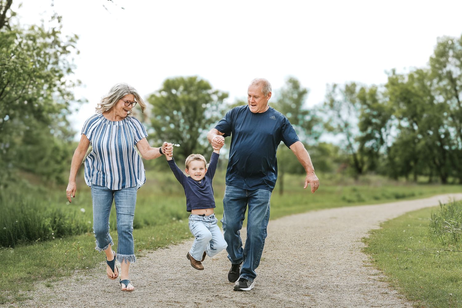 Grandparents joyfully swinging young grandchild between them on an outdoor path.
