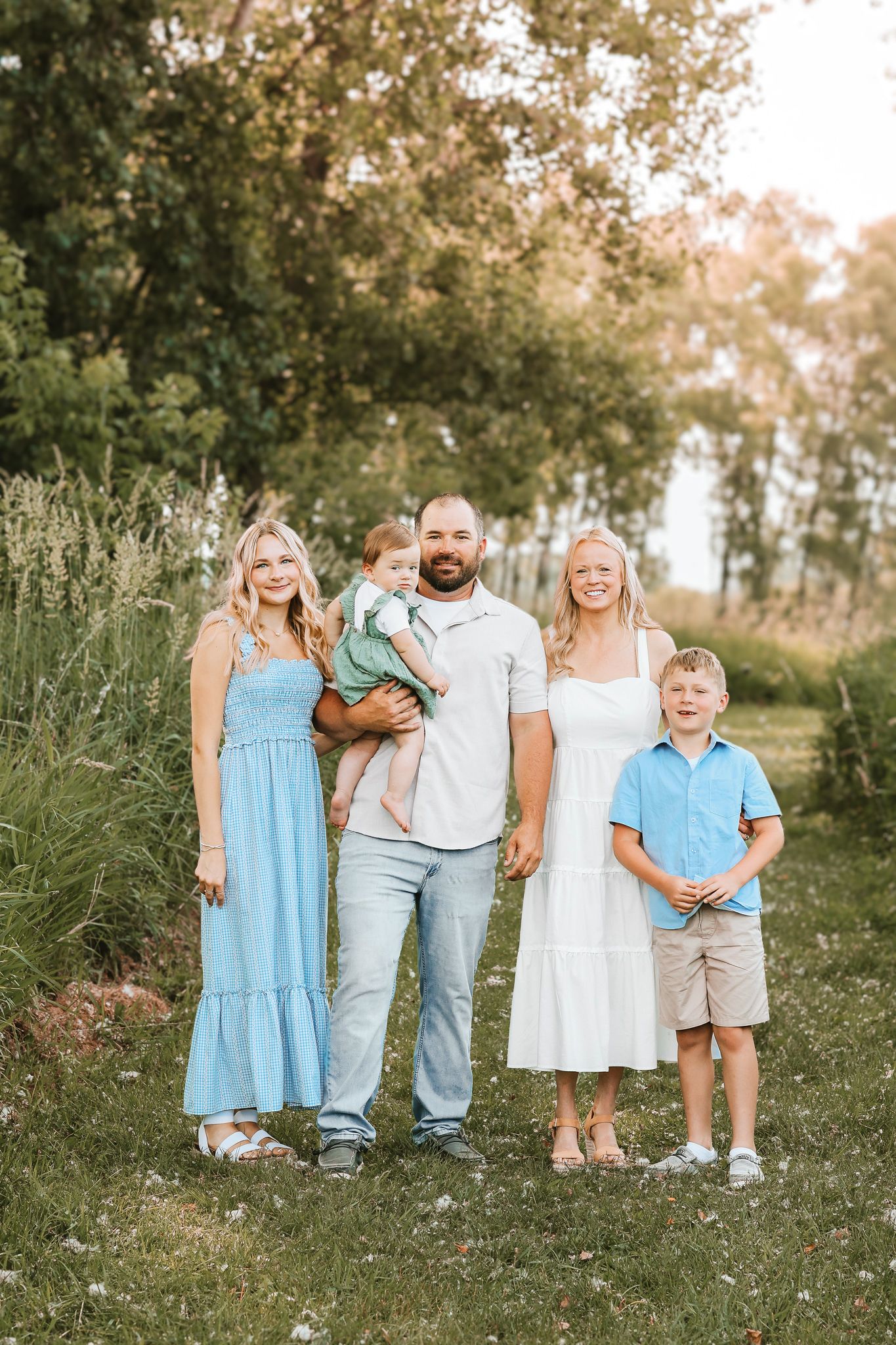 Happy family of five posing outdoors in coordinating blue and white outfits in a lush green field.