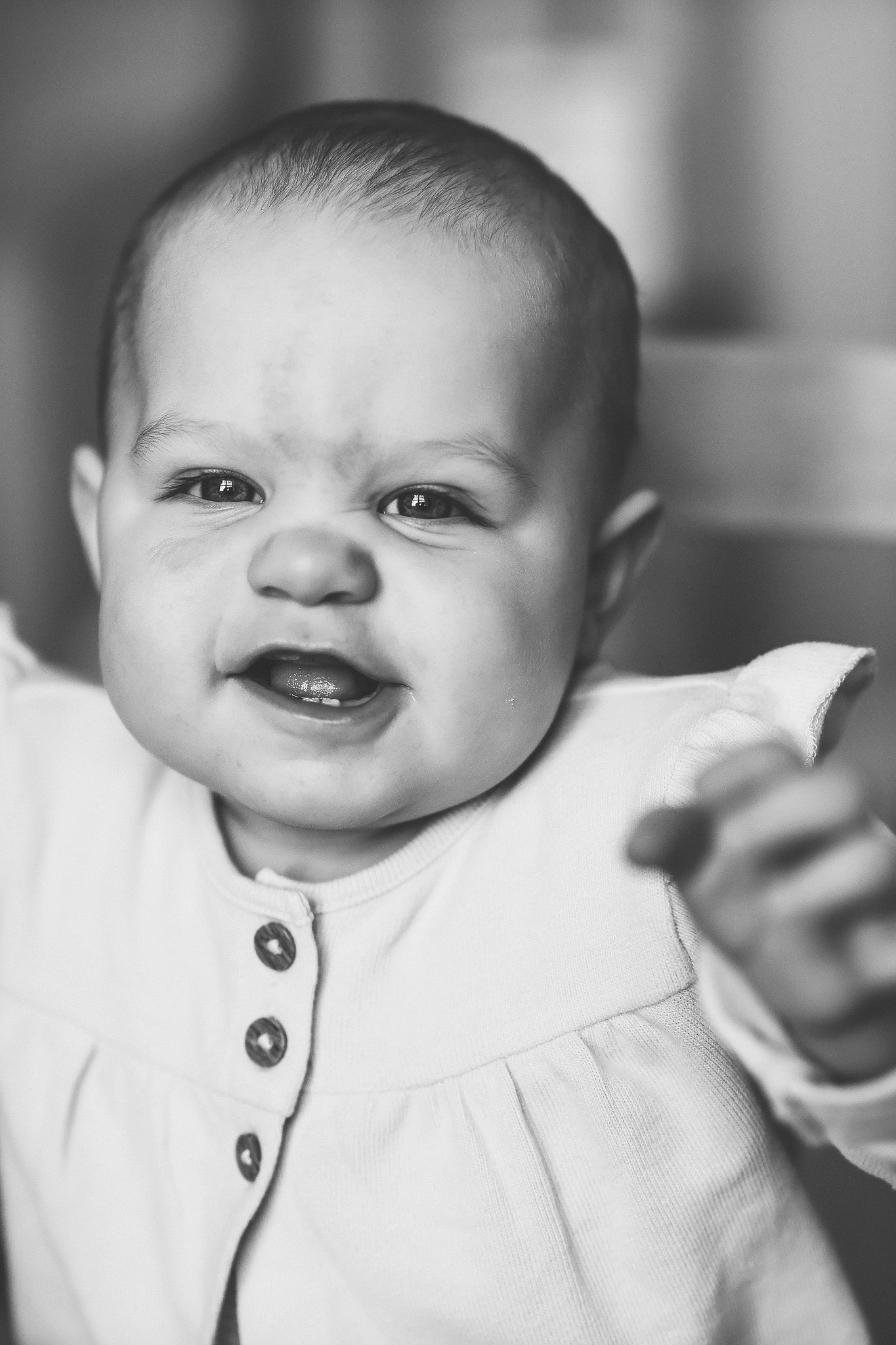 Black and white portrait of a smiling baby reaching toward the camera.