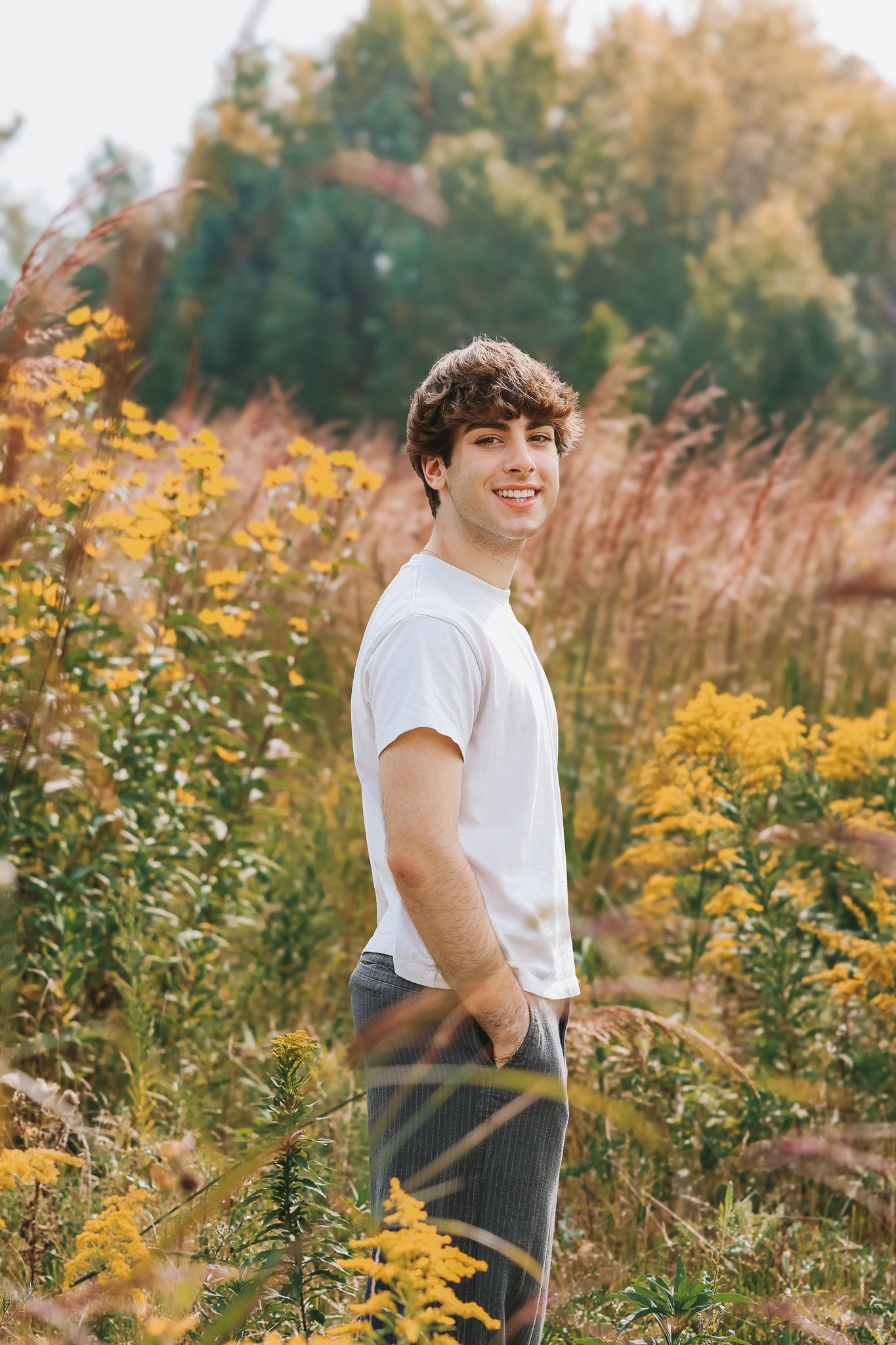 Smiling young man in white t-shirt standing among yellow wildflowers in autumn field.