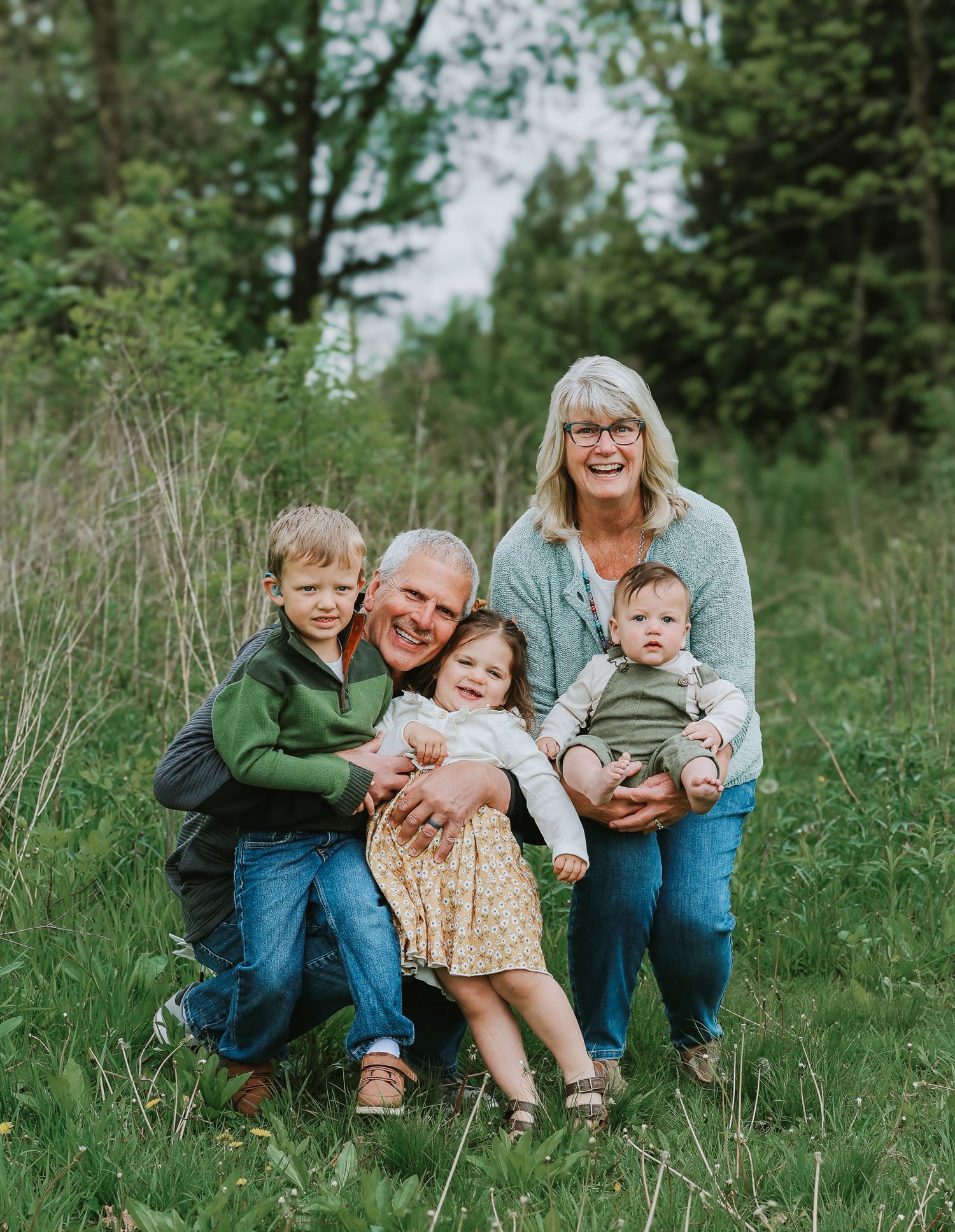 Grandparents pose joyfully with three young grandchildren in a green grassy outdoor setting.