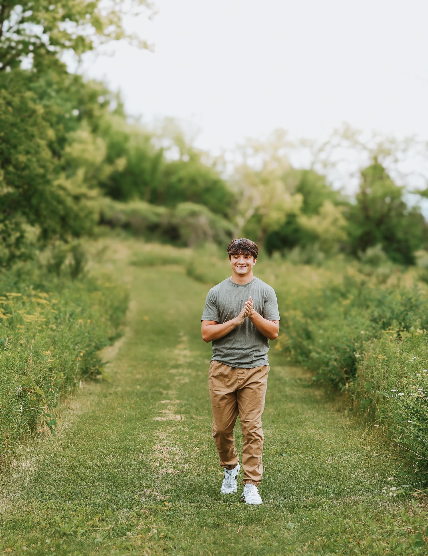 Smiling young man in gray tee and khakis walking down green grassy nature path.