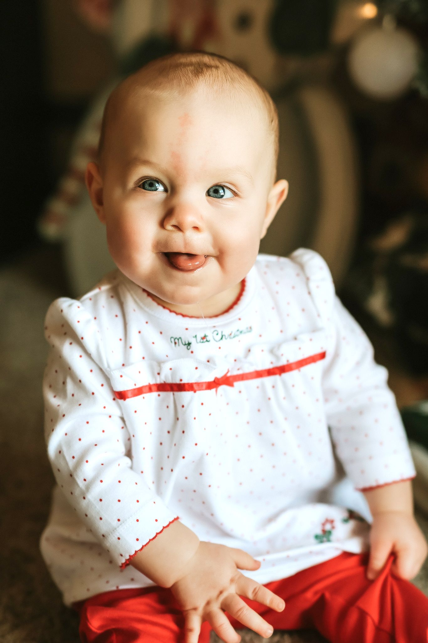 Smiling baby girl wearing a My 1st Christmas white polka dot dress with red trim.