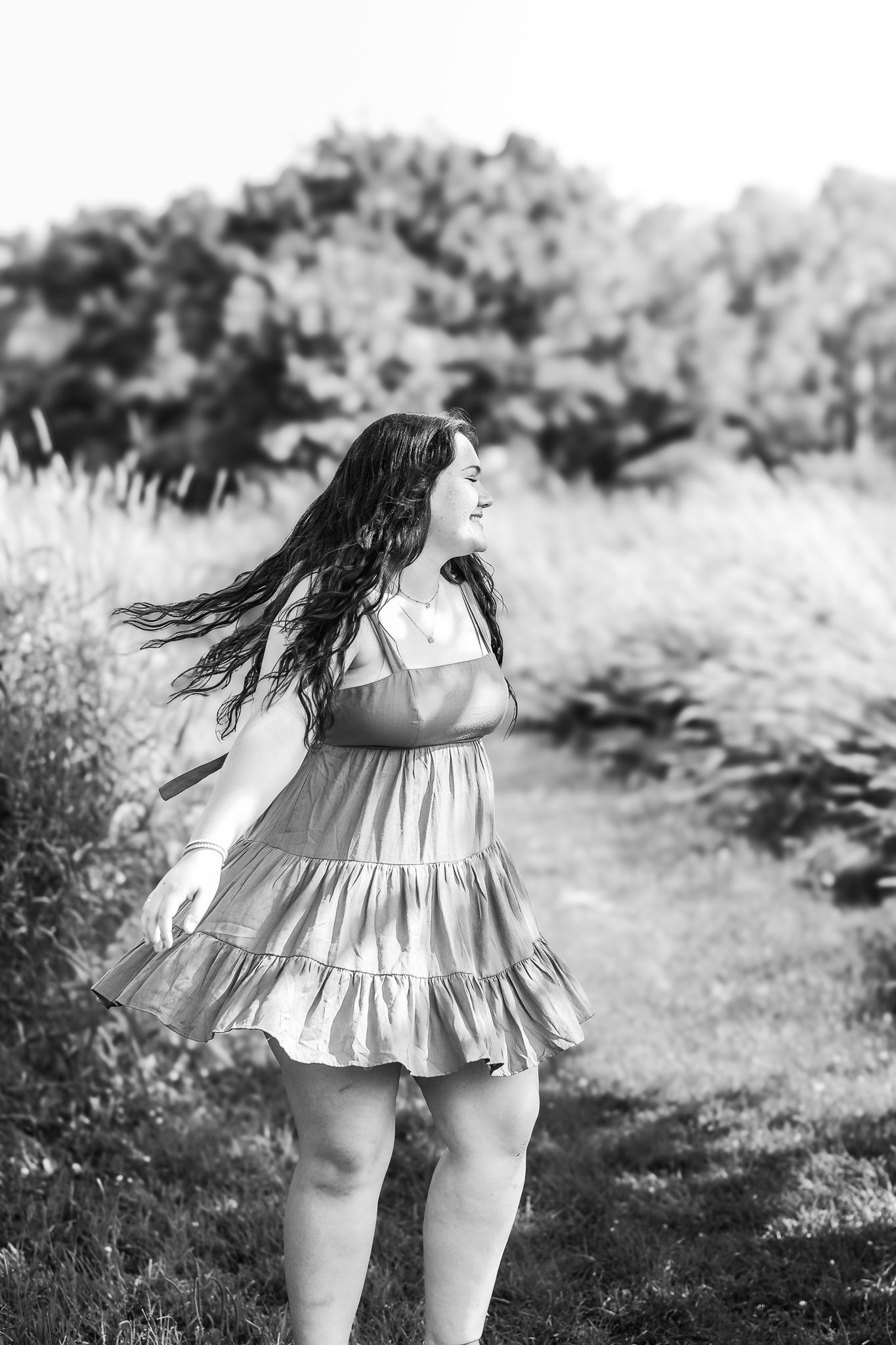 Black and white photo of teenage girl in sundress with hair blowing in wind outdoors.