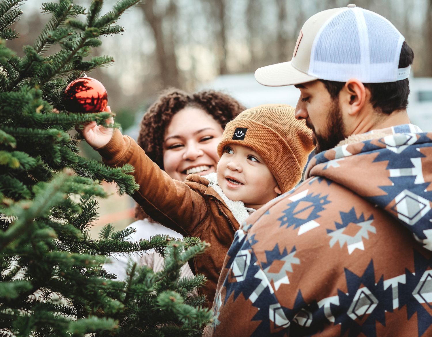 Young family decorating a Christmas tree together with a baby reaching for a red ornament.